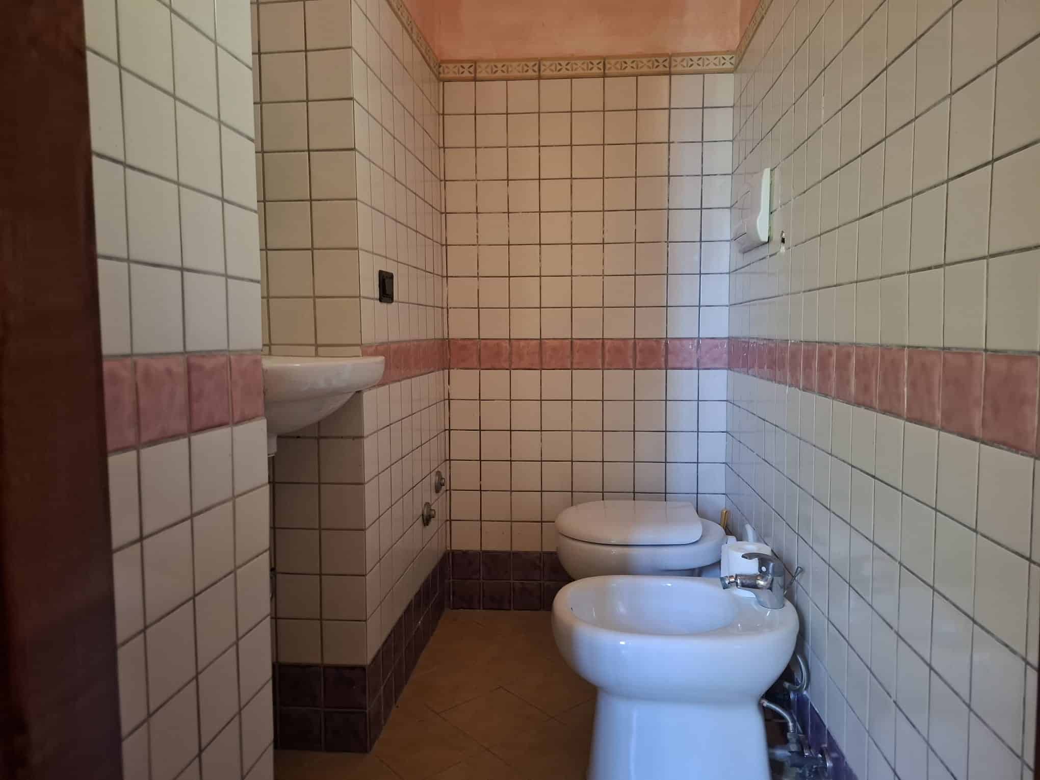 Lavabo e bidet in bagno con piastrelle beige e rosa, spazio funzionale e pulito, ideale per servizi igienici in ambienti residenziali o commerciali.
