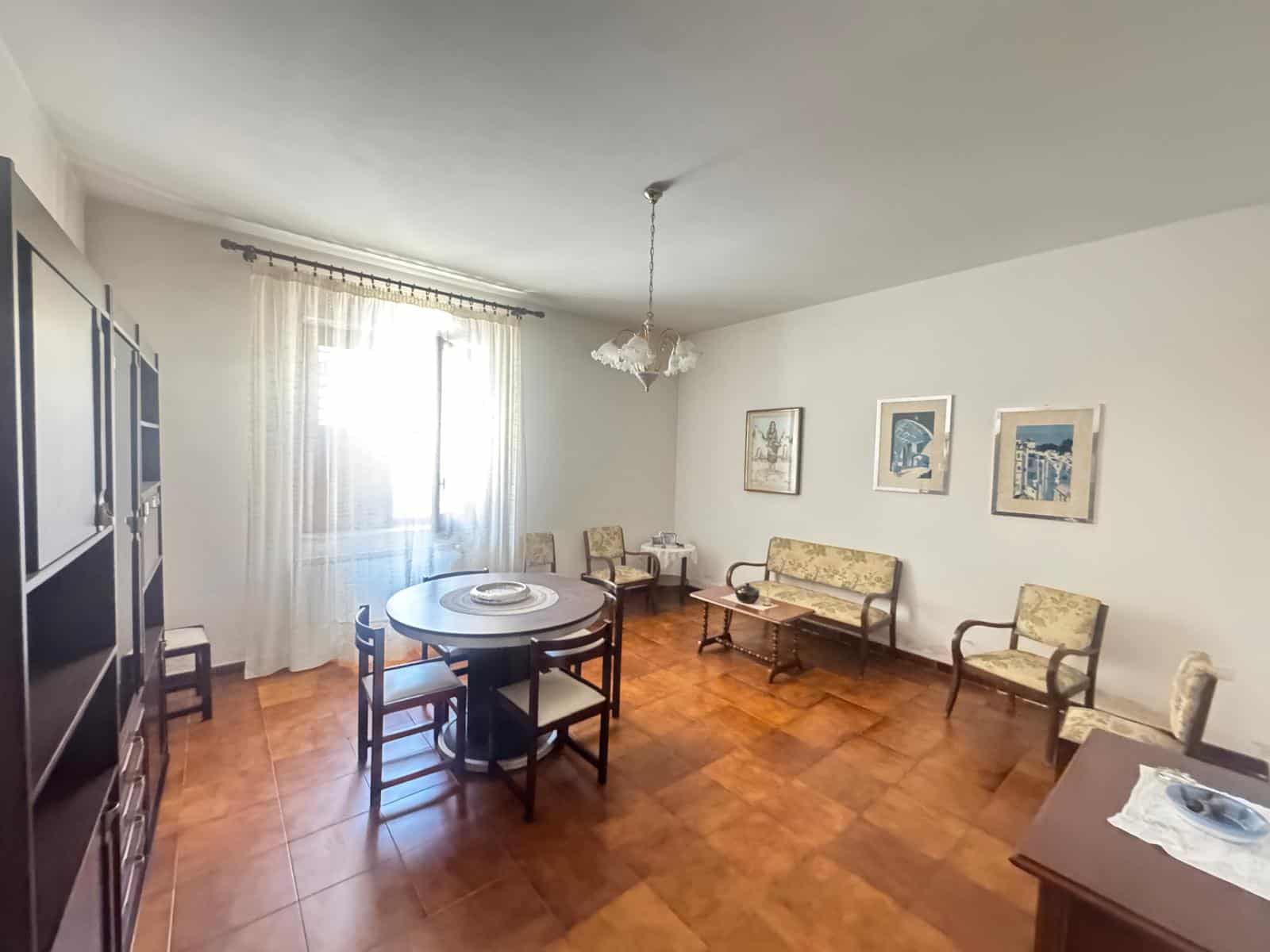 Ampia sala da pranzo con tavolo rotondo, sedie e divani eleganti, illuminata da luce naturale, ideale per incontri familiari e momenti di relax, in un ambiente accogliente e ben arredato.