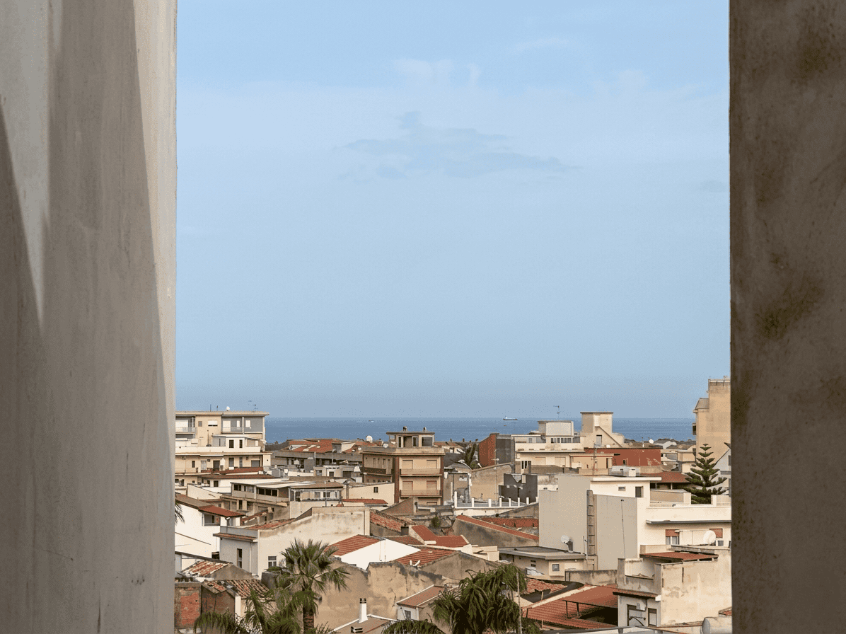 Veduta panoramica di una città costiera con edifici residenziali e il mare sullo sfondo, scattata da un punto elevato con colonne in primo piano.