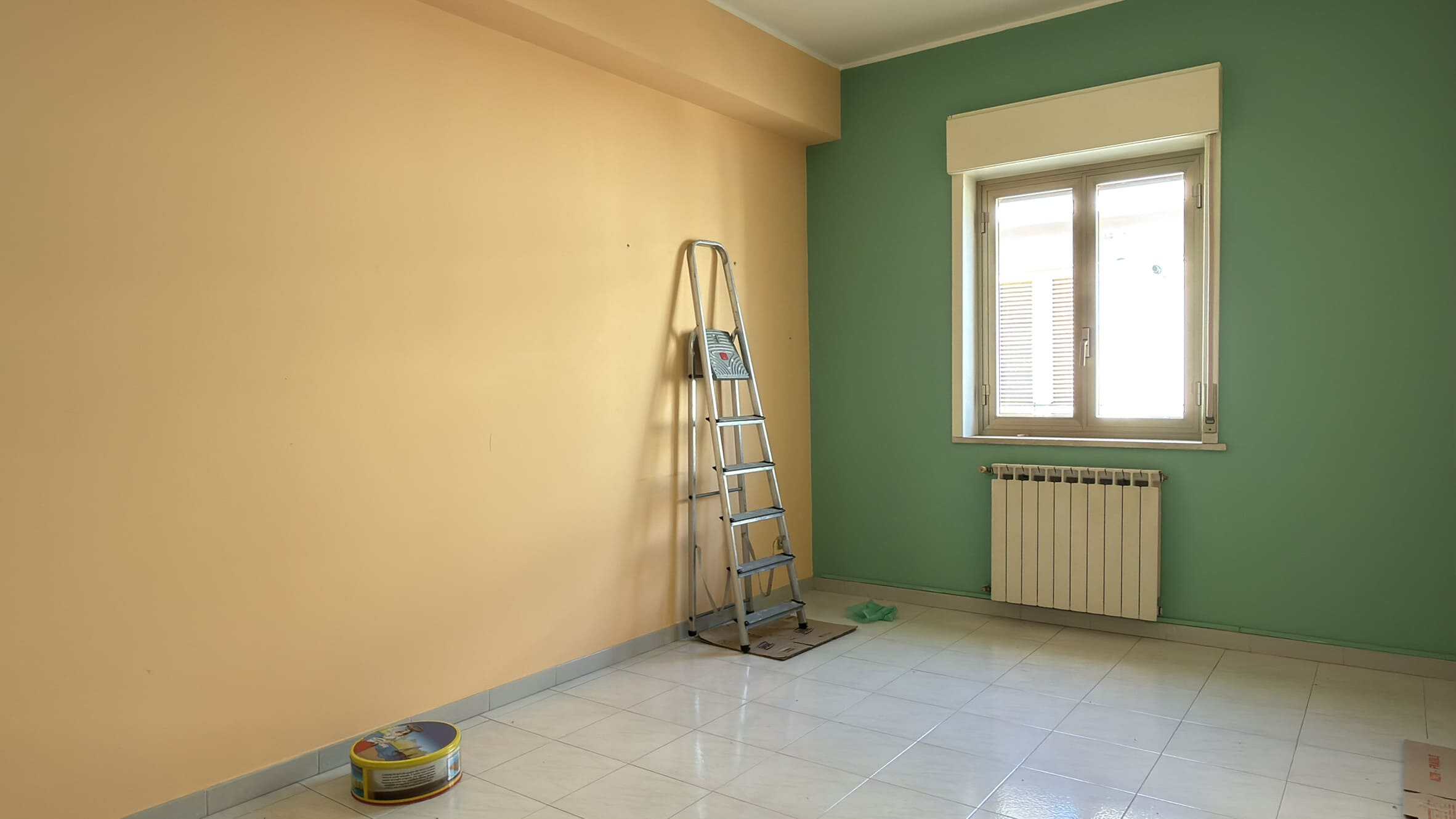 Stanza vuota in fase di ristrutturazione con pareti colorate, finestra e scala in metallo.