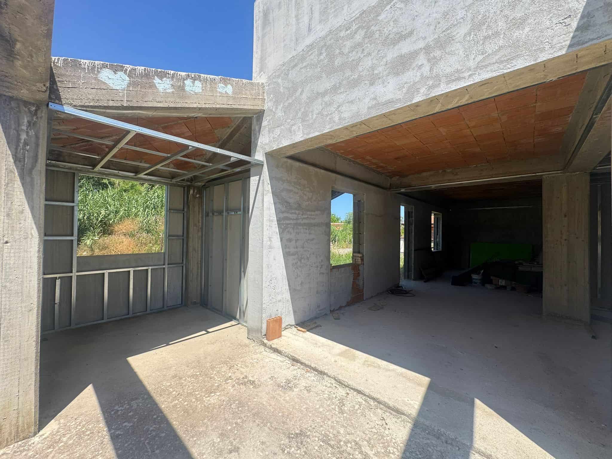 Immagine di una casa in costruzione con pareti in cemento e finestre senza infissi, in fase di completamento.