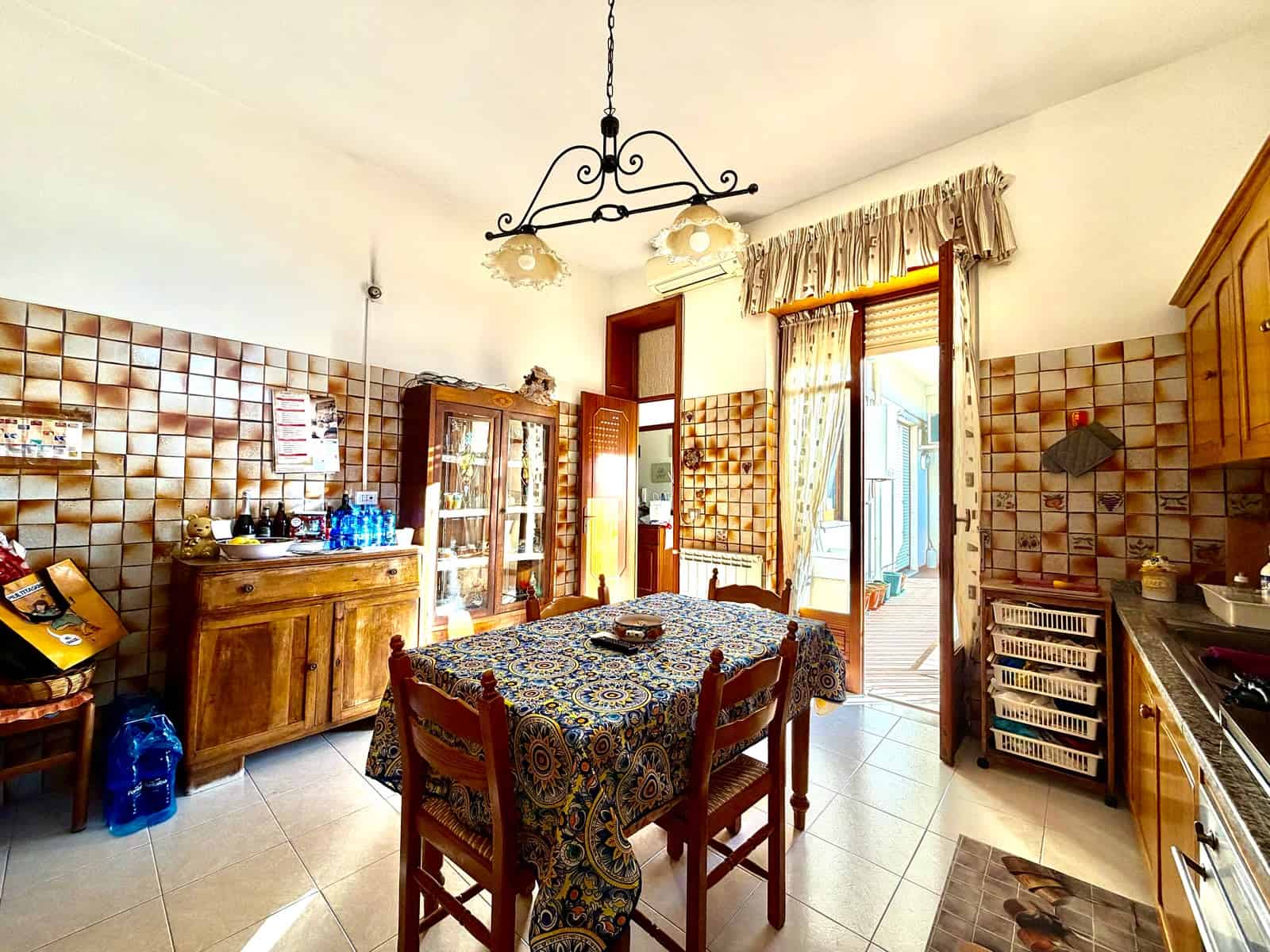 Interno cucina di un appartamento in vendita a Barcellona P.G., con mobili in legno, tavolo con tovaglia, e accessori vari.