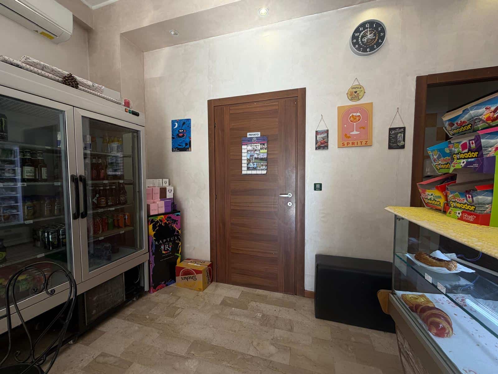 Interno di un negozio con frigorifero, scaffali con snack e decorazioni alle pareti.