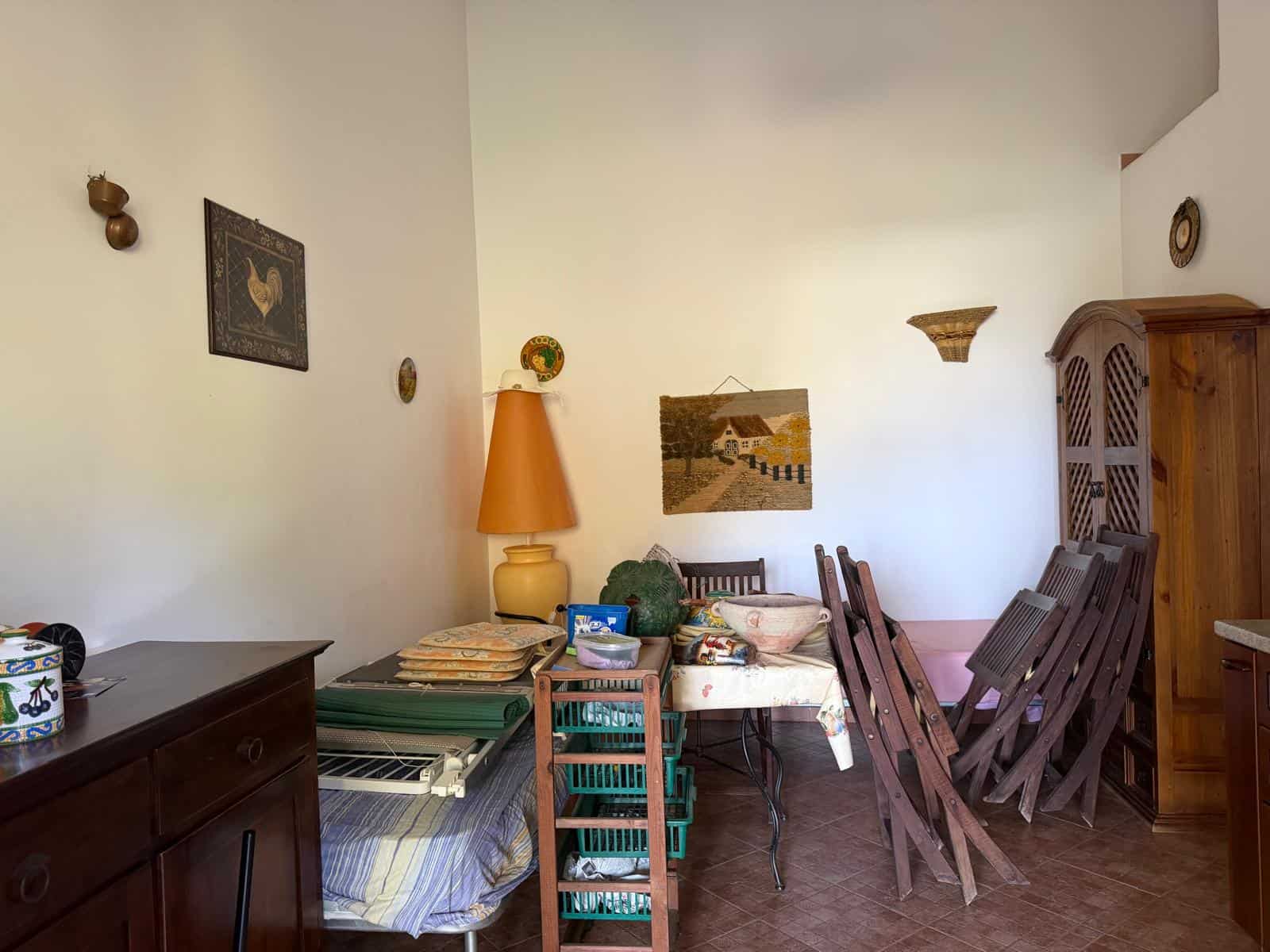 Interno di una stanza con mobili in legno, tavolo con sedie impilate, lampada arancione e decorazioni rustiche, ambiente accogliente e tradizionale.