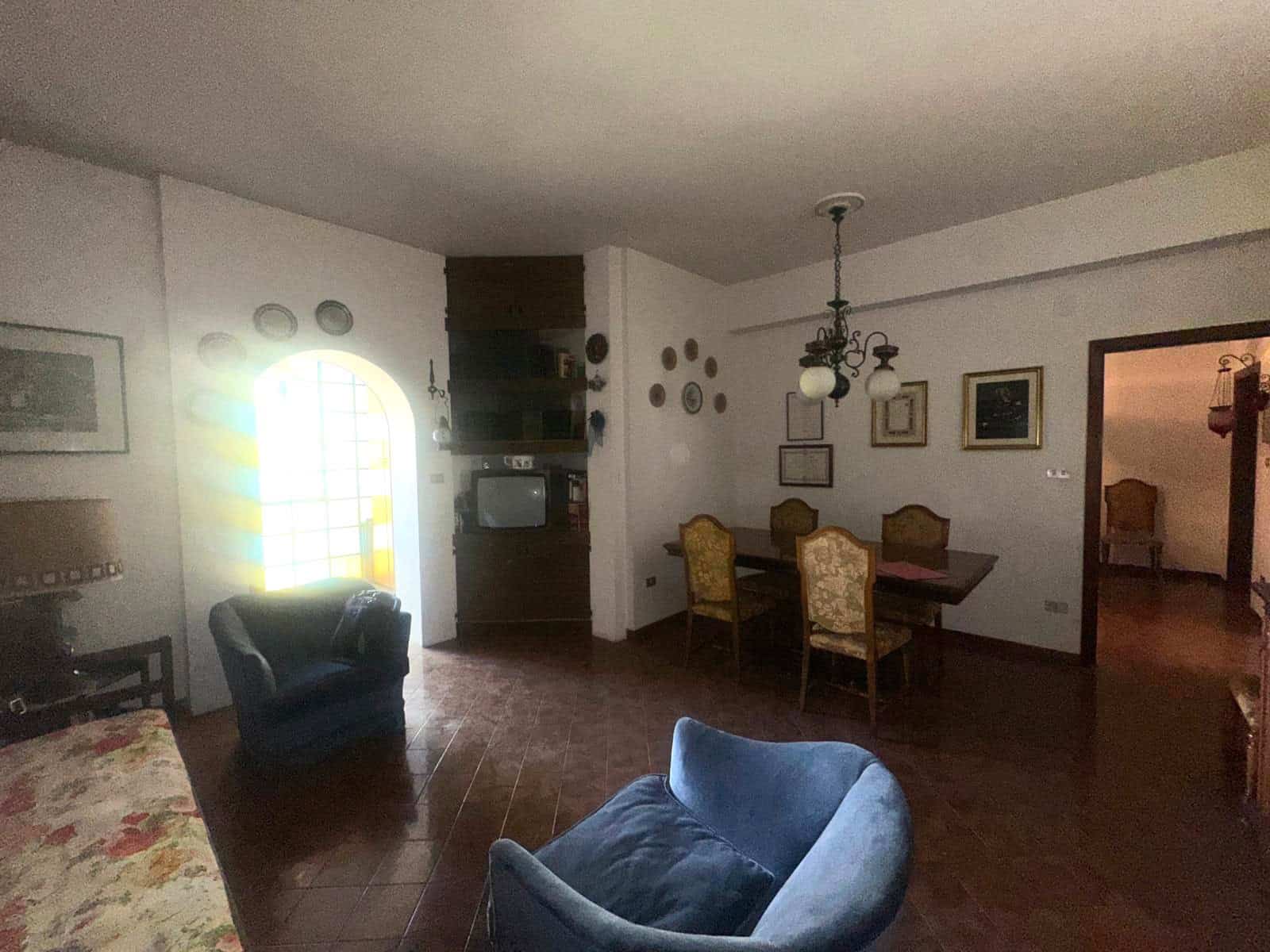 Il soggiorno di una casa spaziosa e accogliente con mobili classici, pareti decorate con quadri e piastrelle in ceramica, illuminato da una lampadiera centrale e luce naturale proveniente dalla finest.