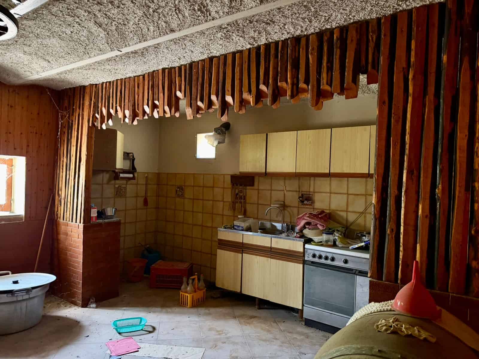 Interno di una cucina rustica con mobili in legno, forno a gas e pareti rivestite di piastrelle beige, ambiente accogliente e informale.