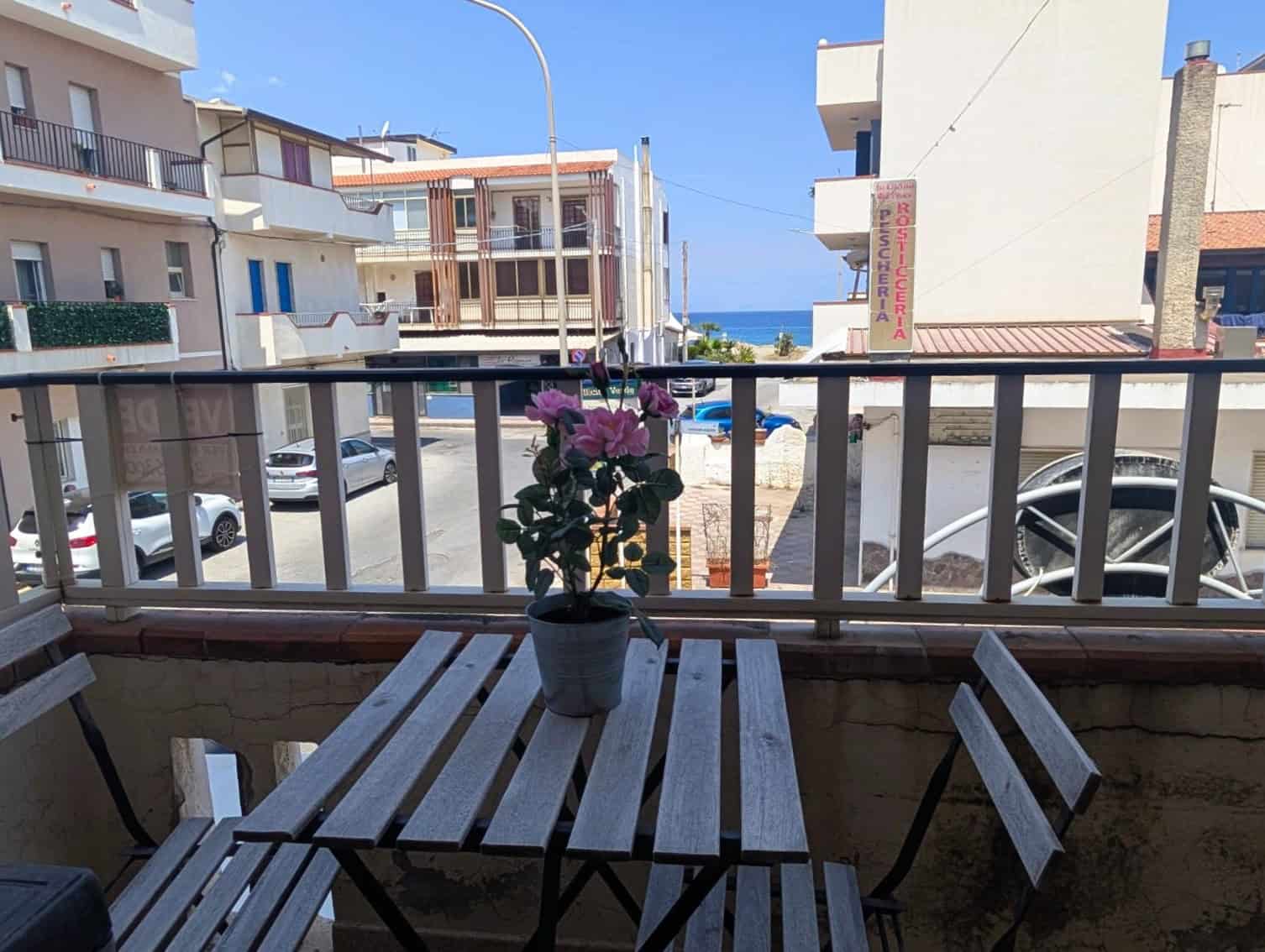Balcone con tavolo e sedie, vista su edifici e mare in lontananza, ambiente esterno tranquillo e accogliente, ideale per relax e momenti di convivialità.