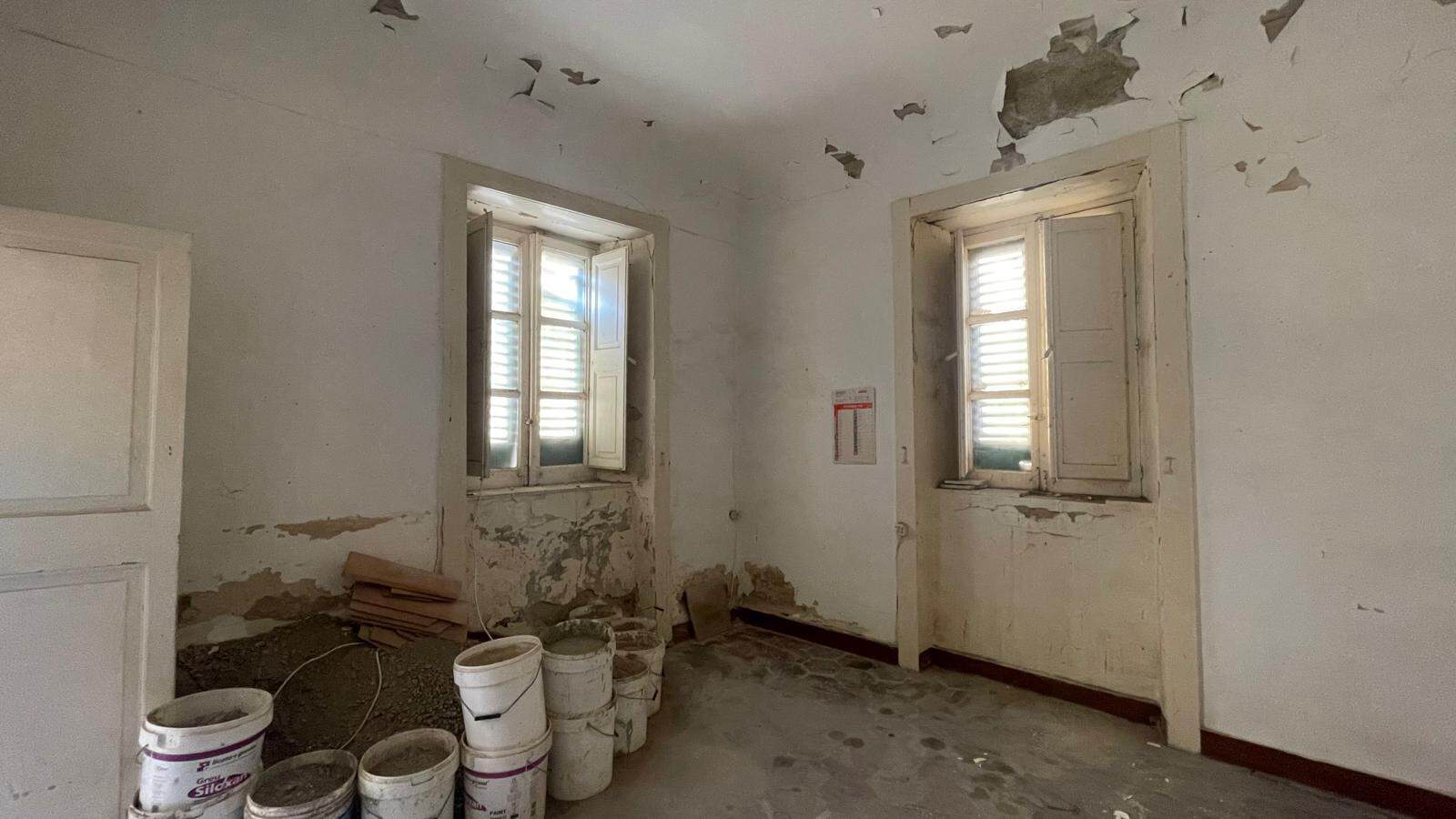 Immagine di una stanza da ristrutturare con pareti danneggiate e finestre vecchie, pronta per lavori di ristrutturazione e riqualificazione edilizia.