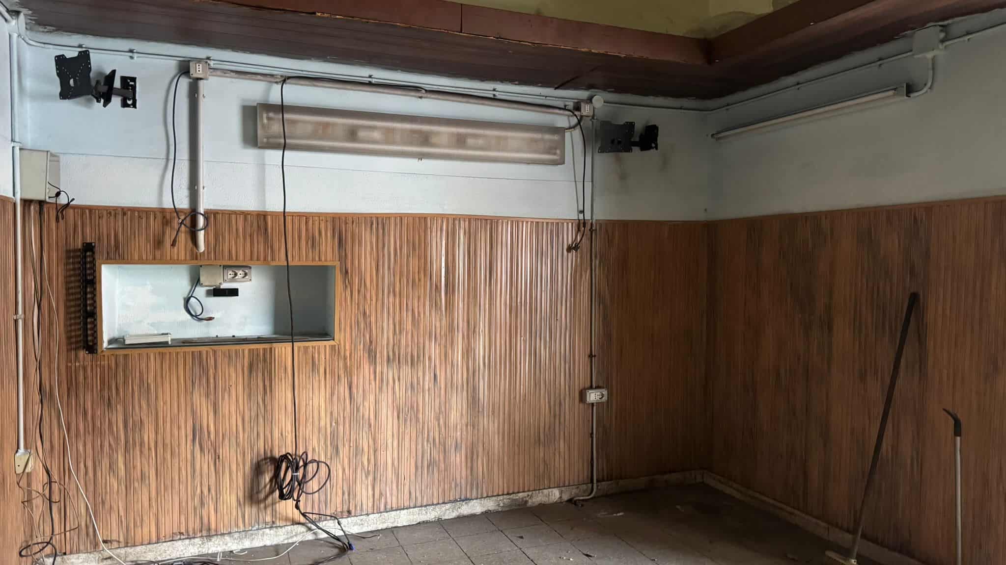 Spazio ufficio senza arredi con pareti in legno e pavimento in cemento, pronto per personalizzazione e allestimento. Ideale per creare un ambiente di lavoro funzionale e accogliente.