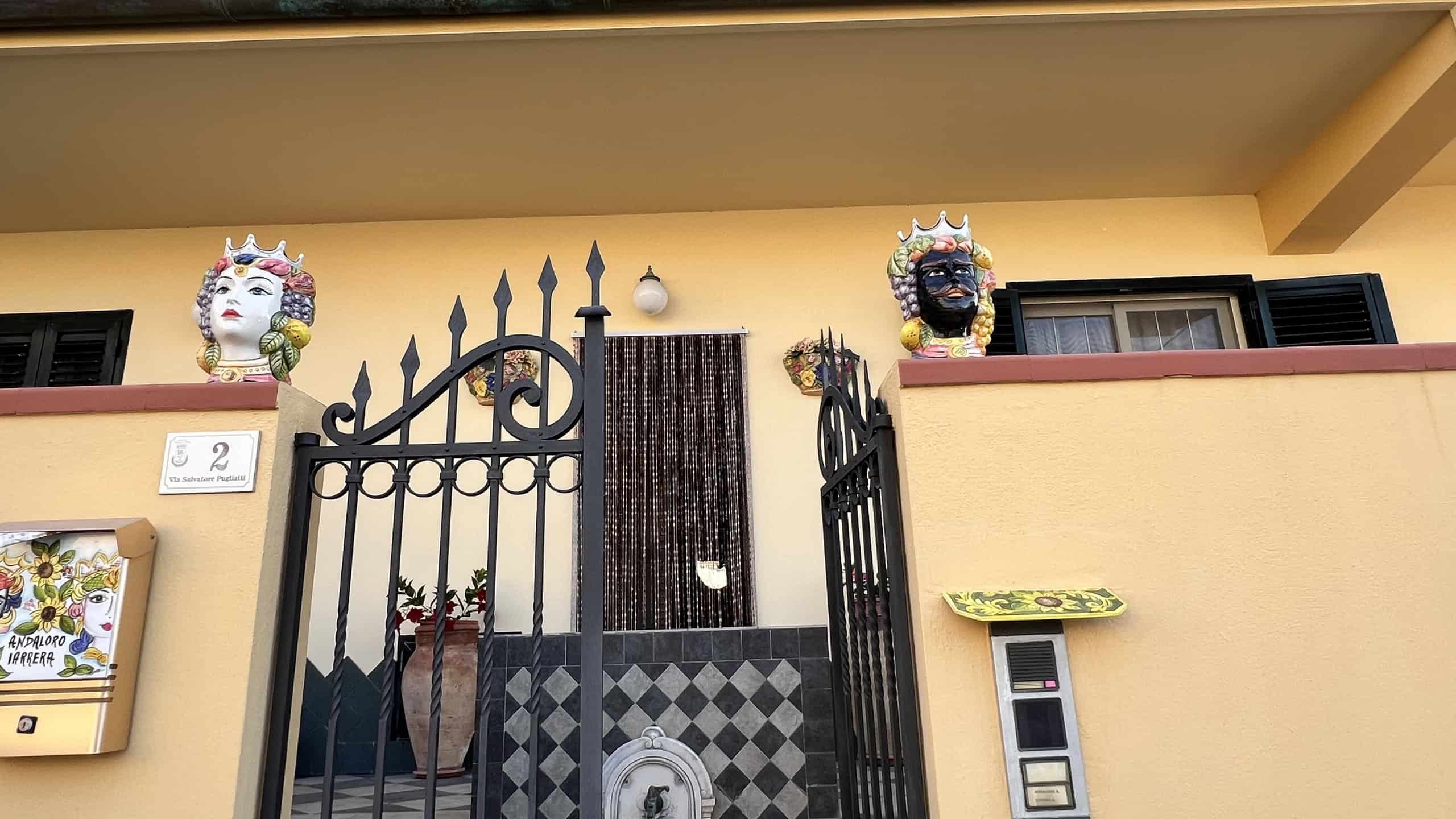Ingresso di una villa unifamiliare con cancellata in ferro battuto e decorazioni colorate sulle pareti esterne.