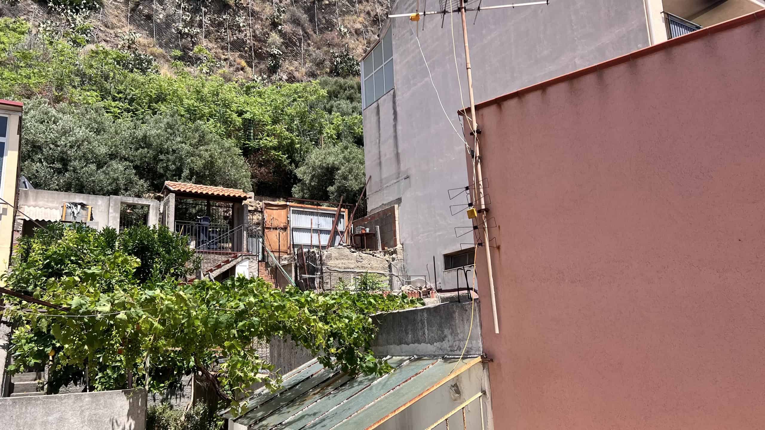 Edificio residenziale in zona collinare con vegetazione e strutture di case vicine a Scaletta Zanclea, Me.