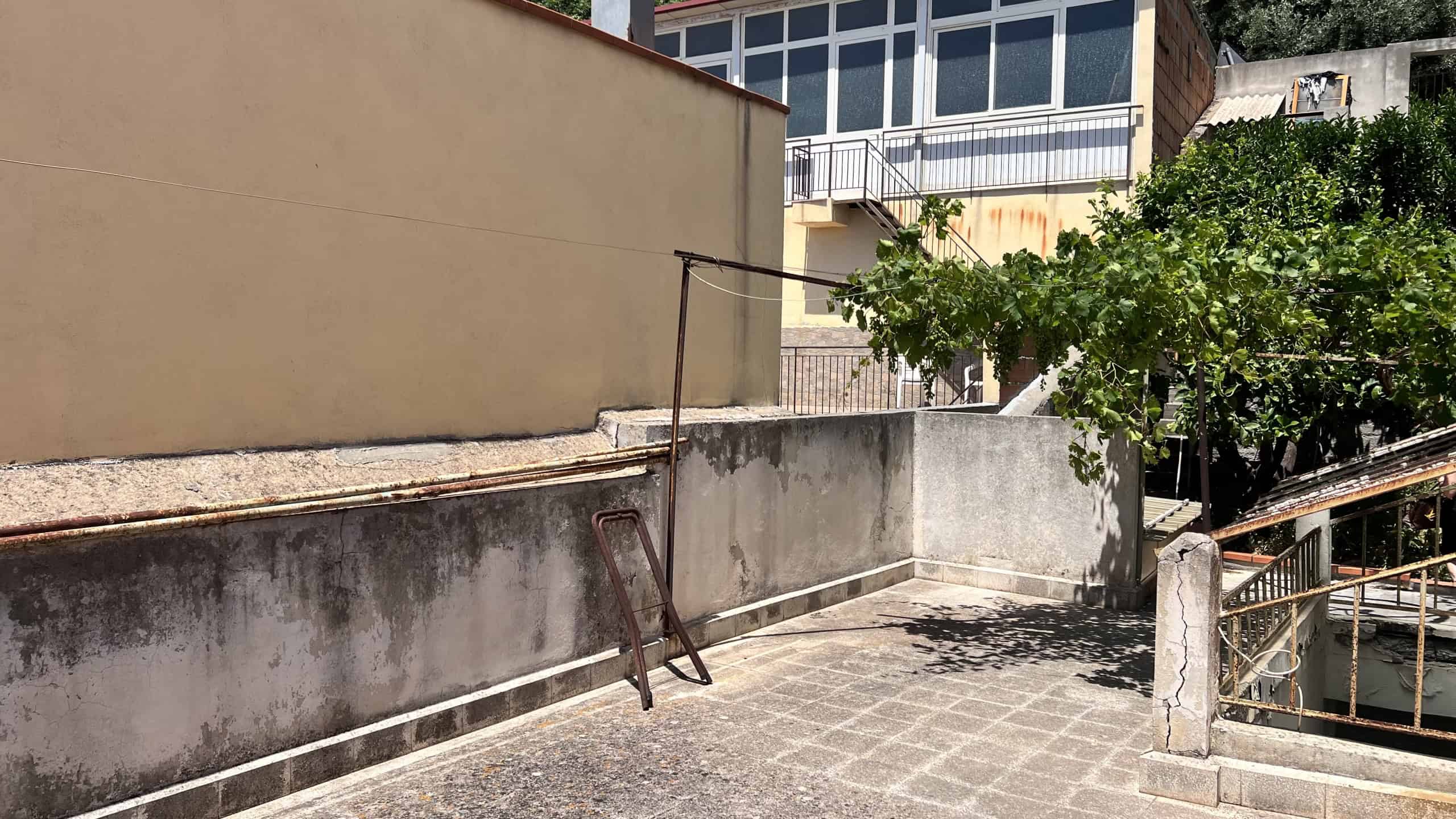 Balcone di un appartamento con vista sulla città, con ringhiera in metallo e piante verdi.