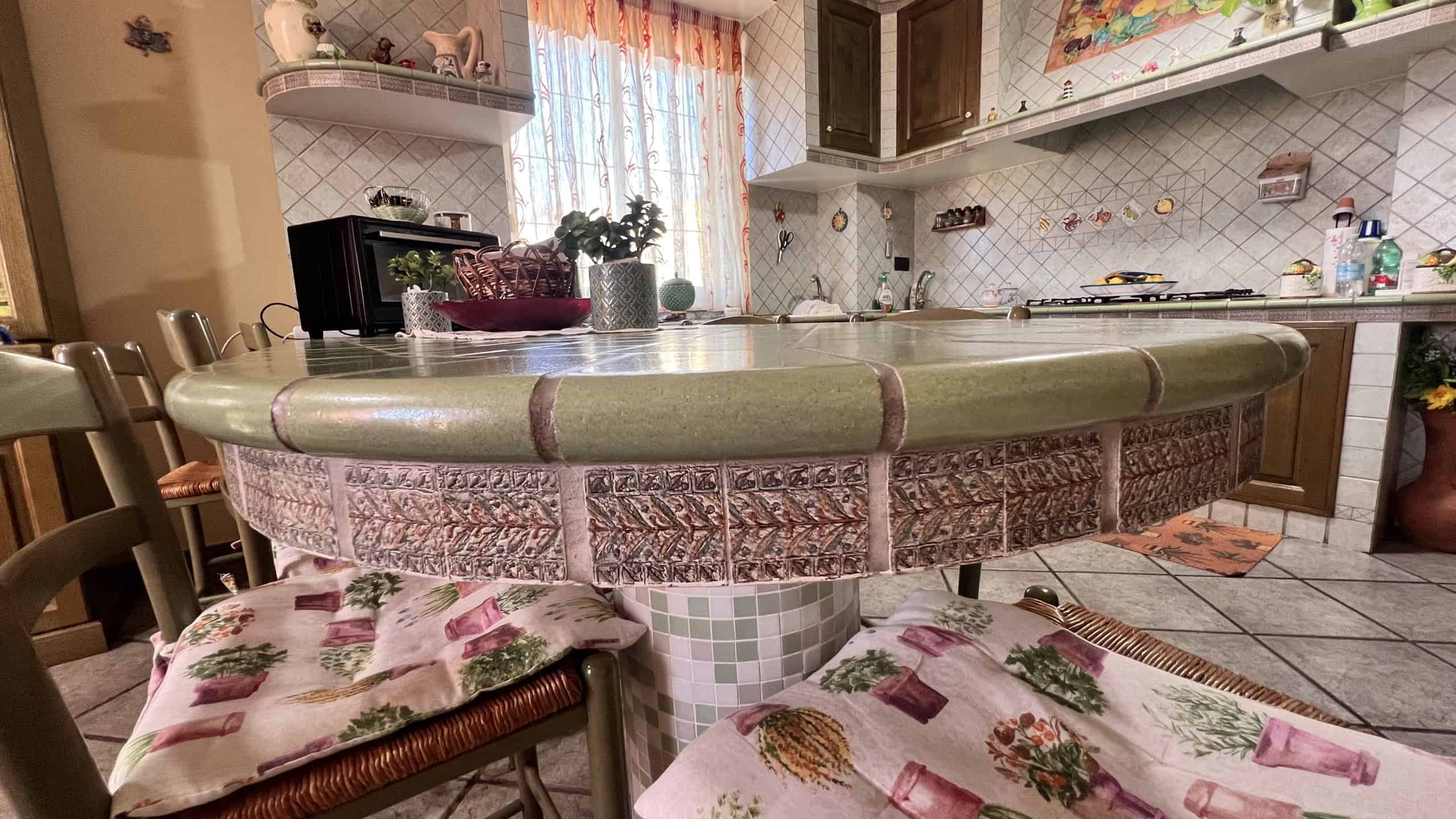 Cucina abitabile con tavolo rotondo in pietra e sedie imbottite, cucina moderna con mobili in legno e pareti decorate.