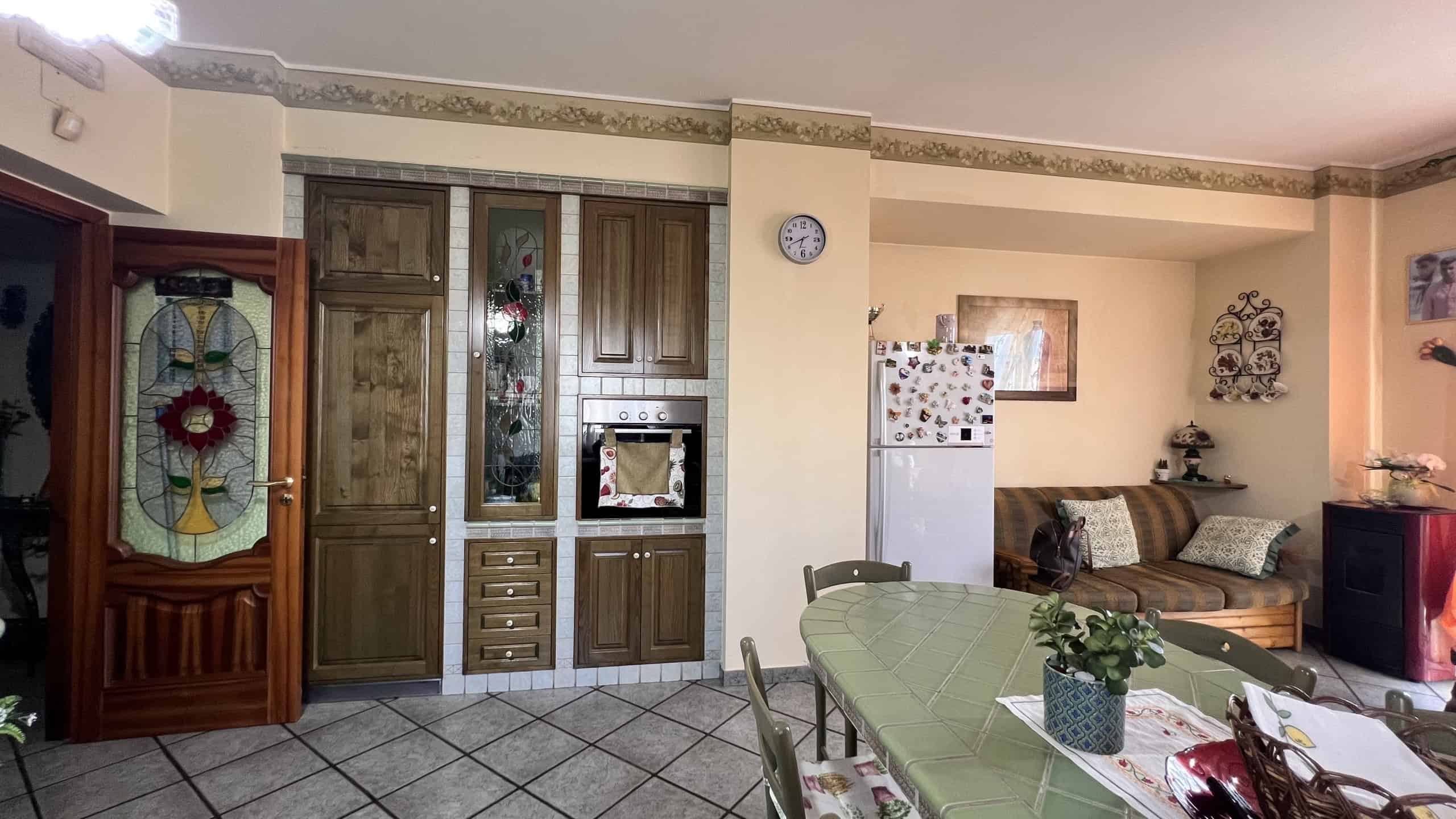 Interno di una casa con cucina e zona pranzo, mobili in legno e decorazioni colorate.