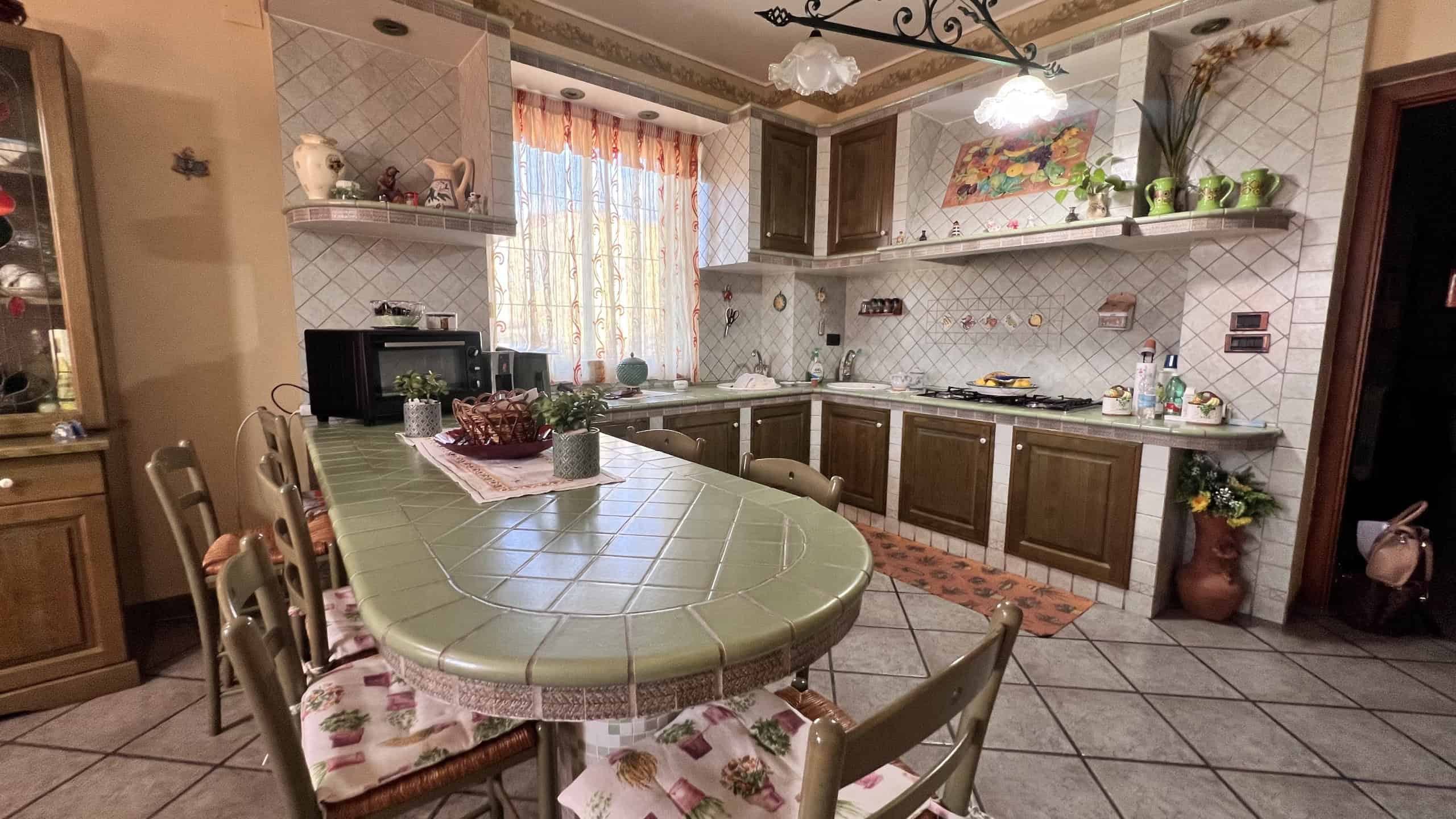 Cucina spaziosa e accogliente con mobili in legno, tavolo centrale e decorazioni floreali, ideale per vivere in una villa in vendita a Villafranca Tirrena.