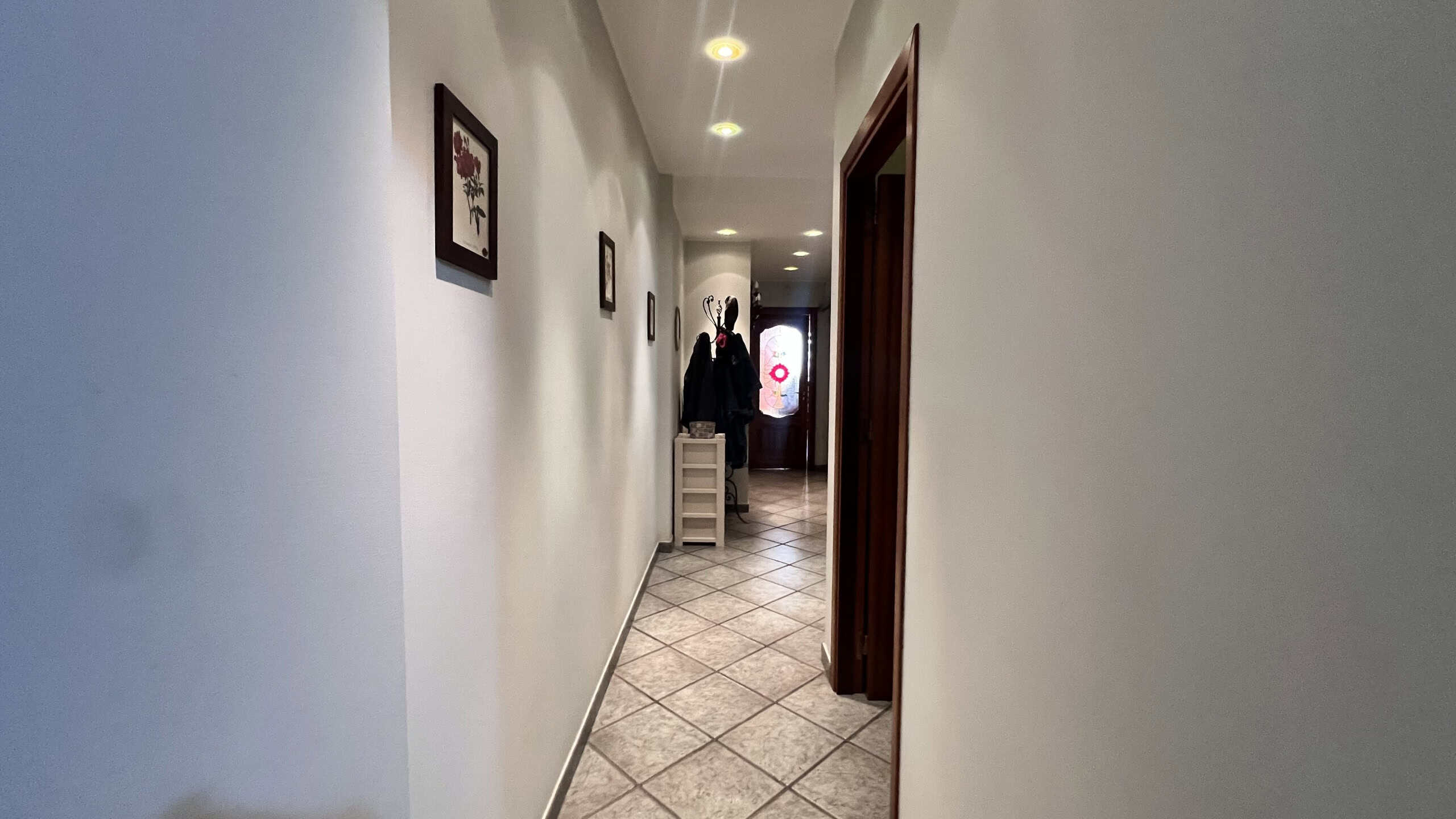 Interno di una villa unifamiliare con pareti bianche, quadri alle pareti e pavimento in piastrelle diagonali.