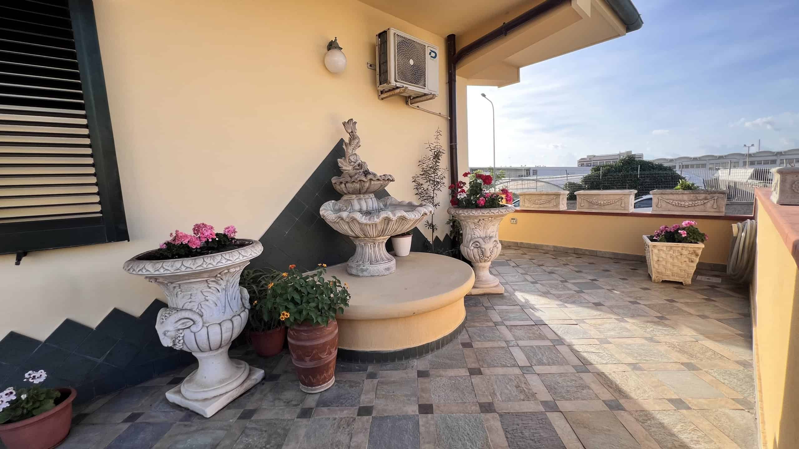 Terrazza panoramica con piante e decorazioni in stile classico, vista sulla città di Villafranca Tirrena.