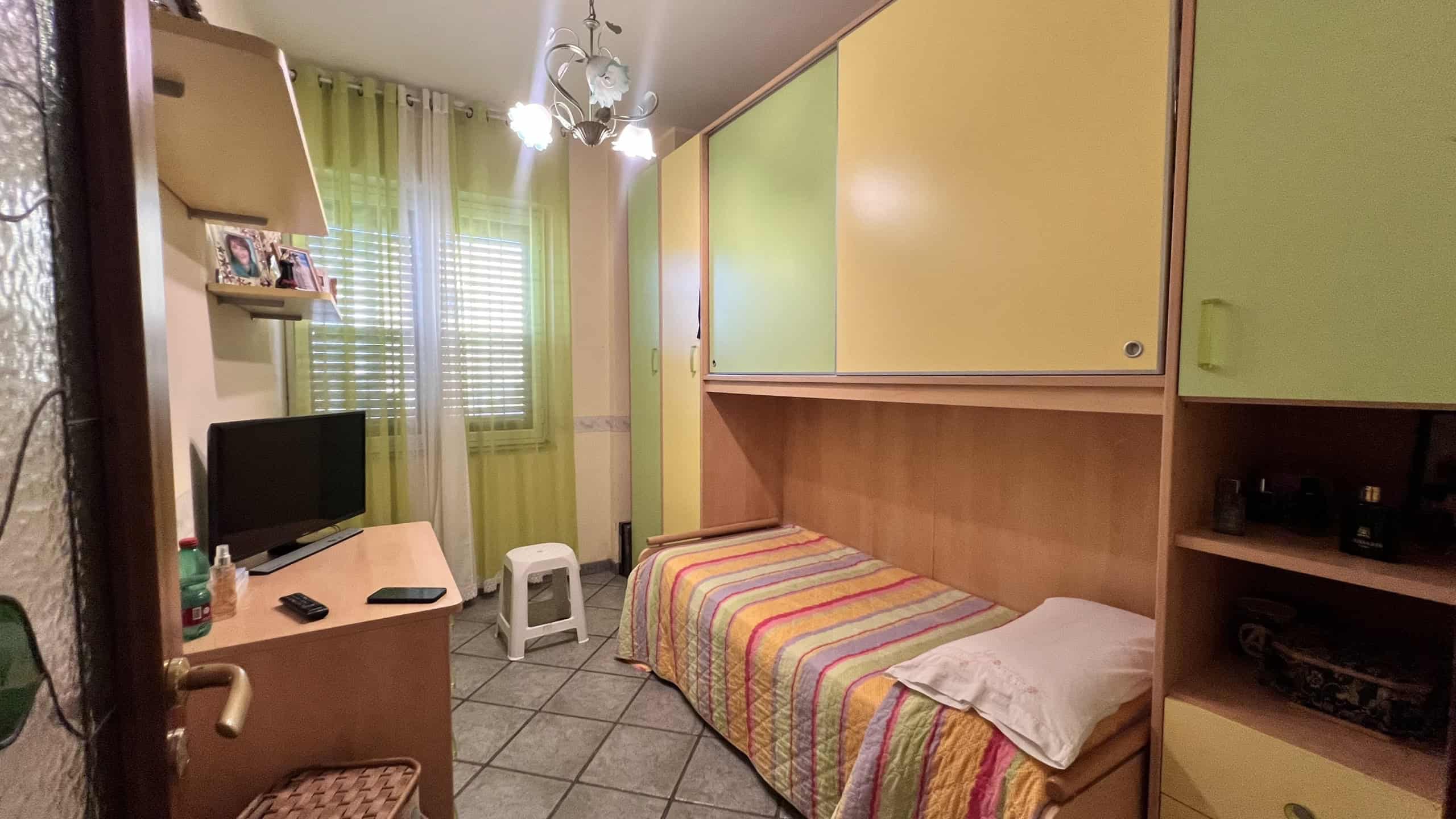 Camera da letto con letto singolo, armadio colorato e finestra con tende verdi, ambiente luminoso e accogliente.