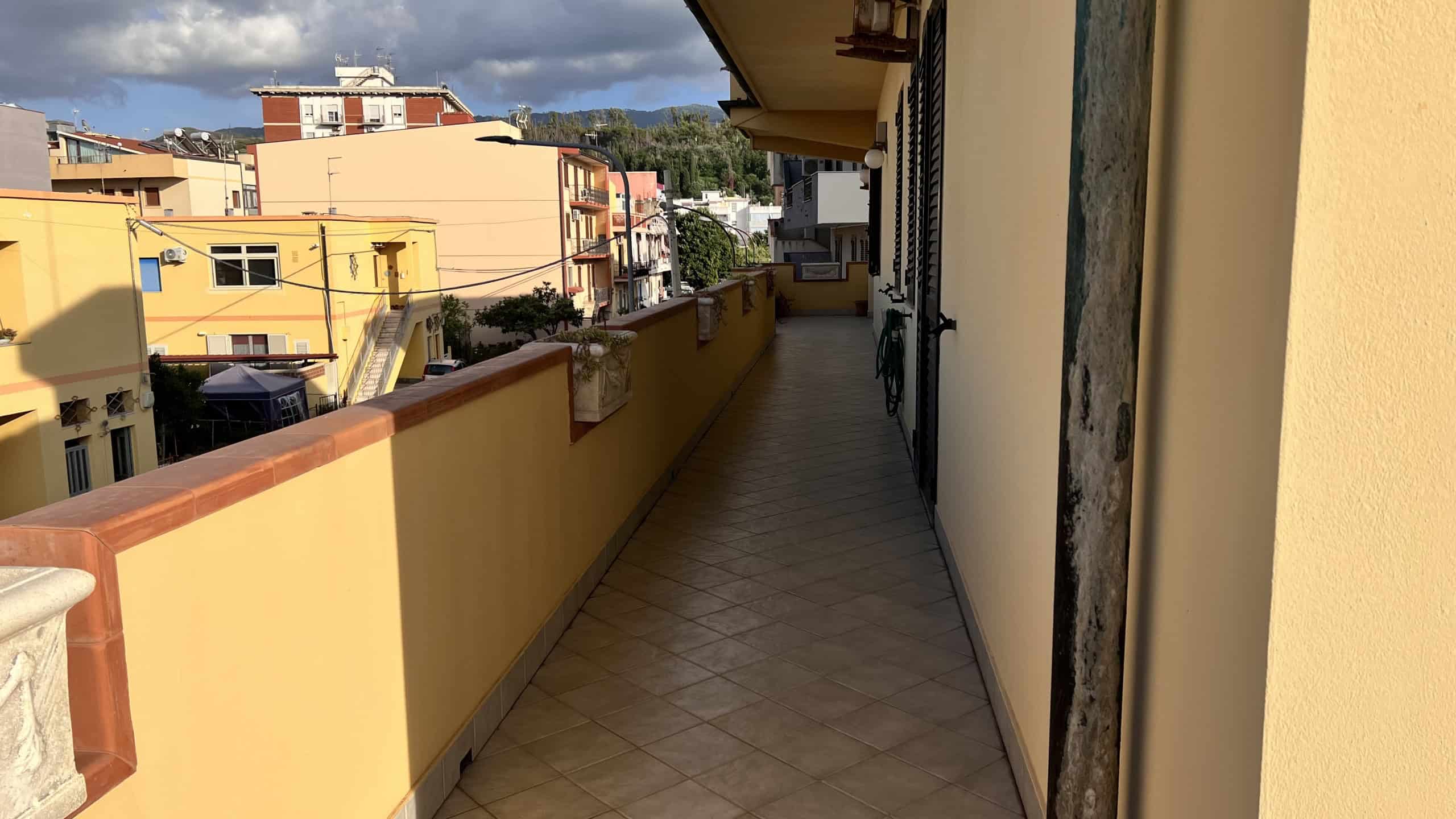 Balcone di un appartamento con vista sulla città di Villafranca Tirrena, in Sicilia, con edifici colorati e cielo sereno.