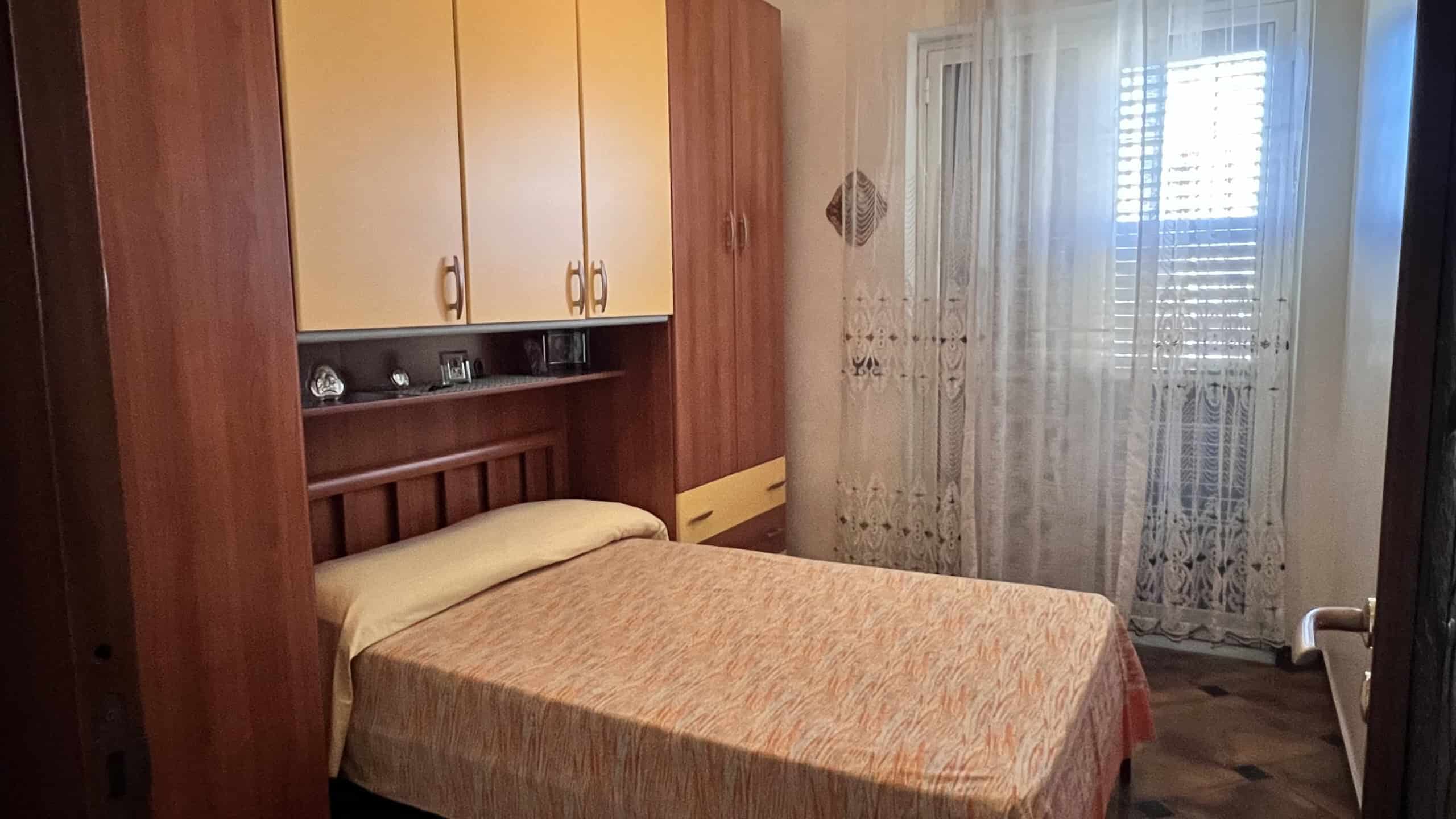 Camera da letto in una villa unifamiliare con armadio a muro e finestra con tende leggere.