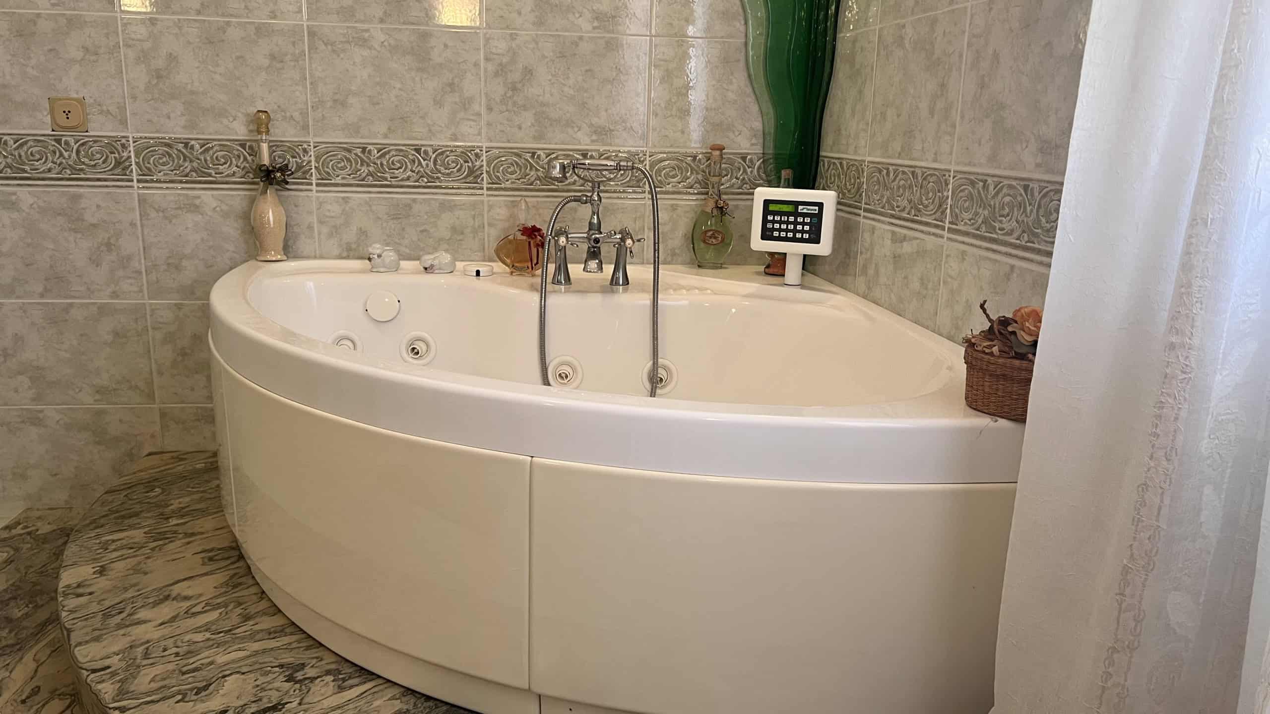 Vasca da bagno angolare in un bagno con pareti rivestite in piastrelle beige e decorazioni decorative.