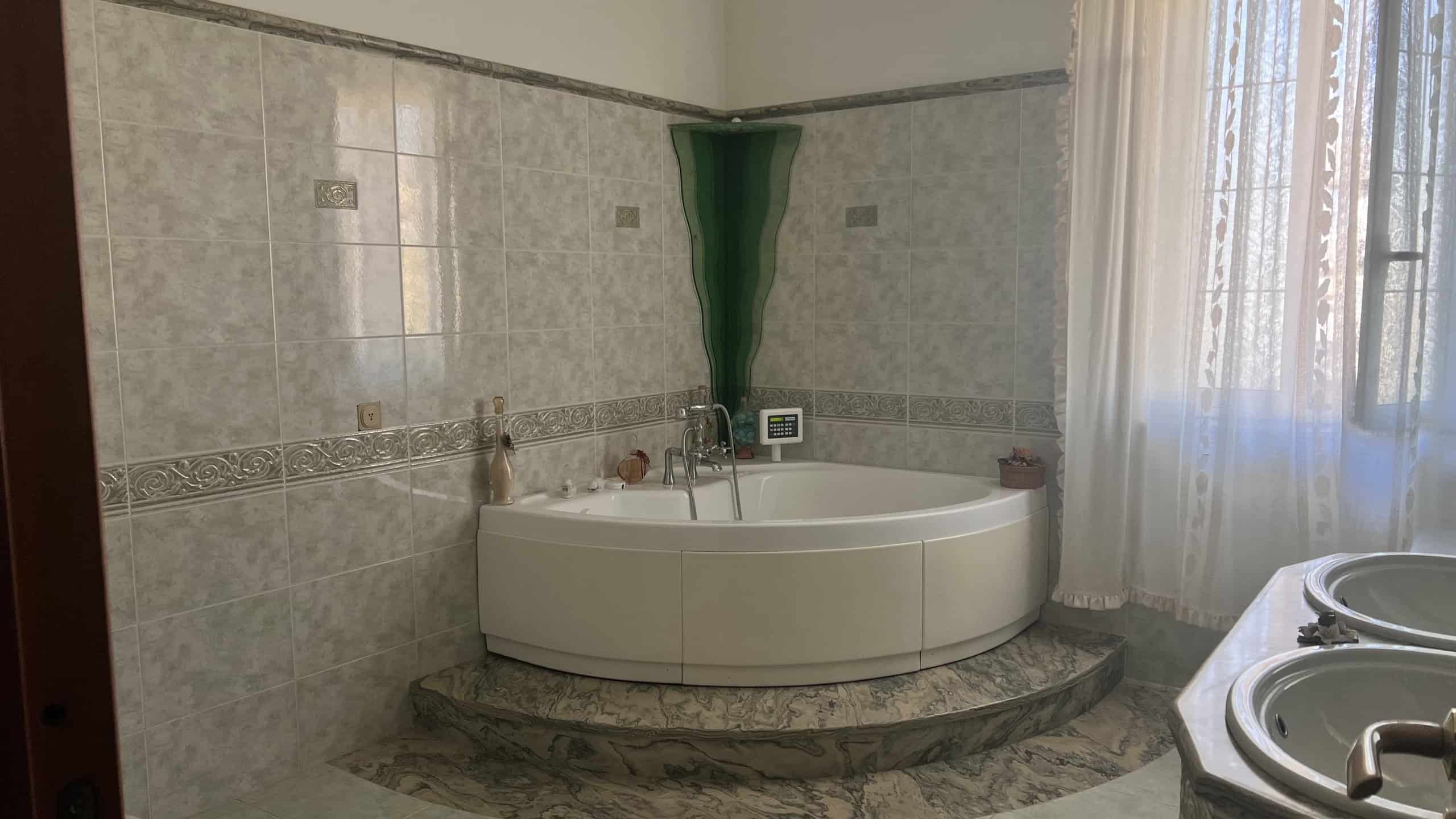 Bagno con vasca idromassaggio rotonda, pareti piastrellate e finestra con tende leggere.