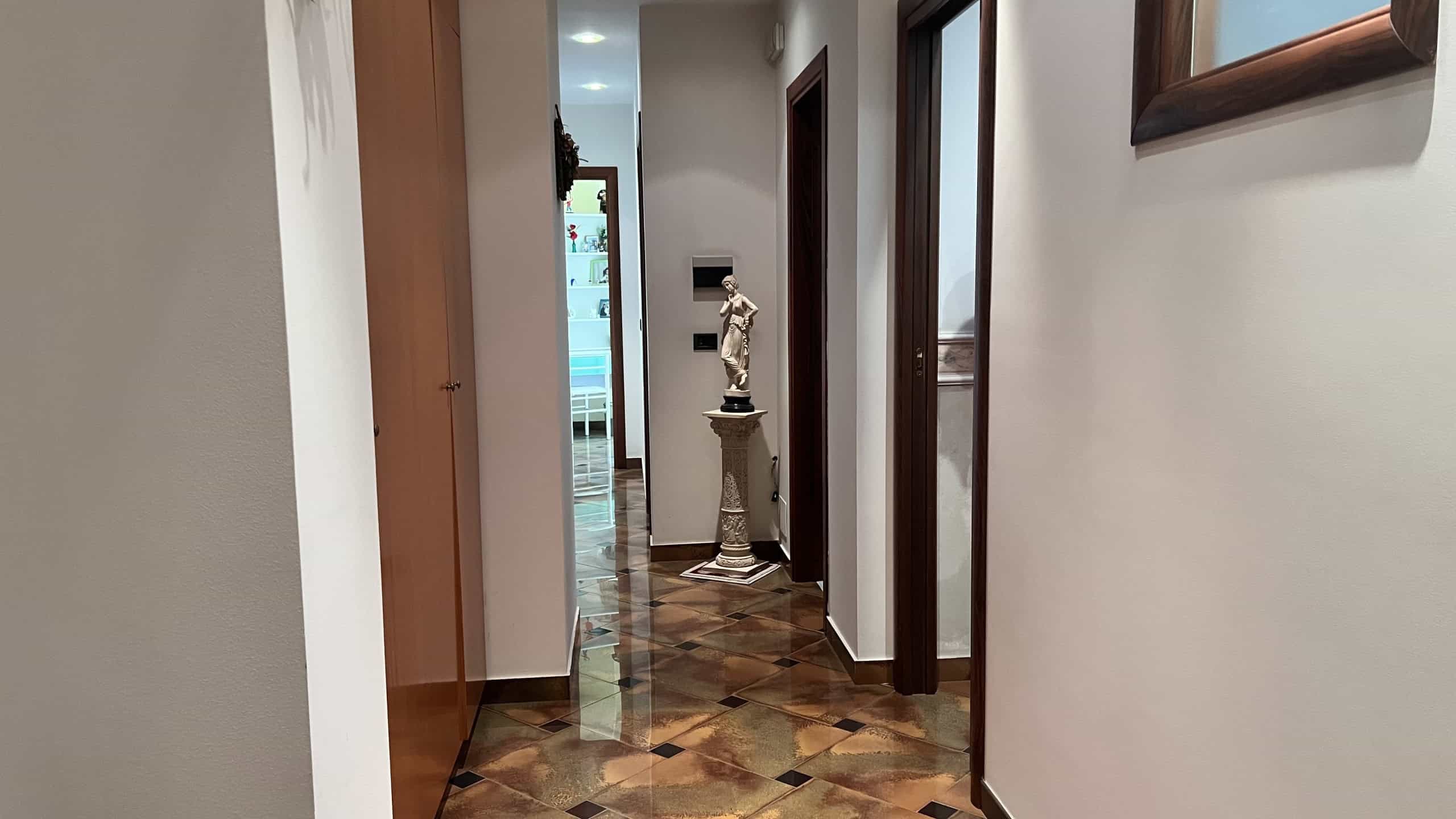 Interno di una villa con pavimento in parquet, pareti bianche e porte in legno, decorato con una statua in un angolo.