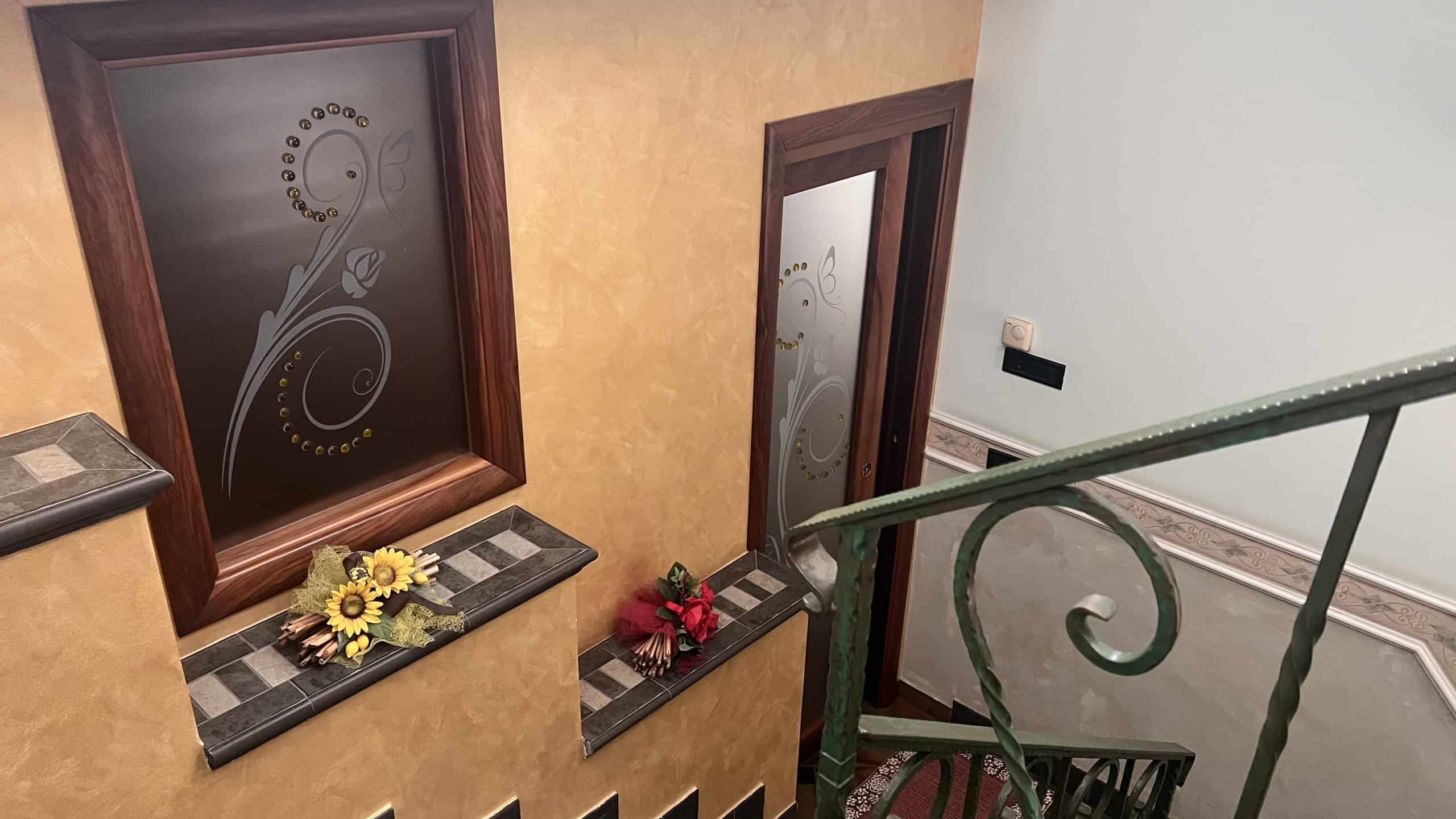 Interno di una scala di una villa con decorazioni floreali e specchi.