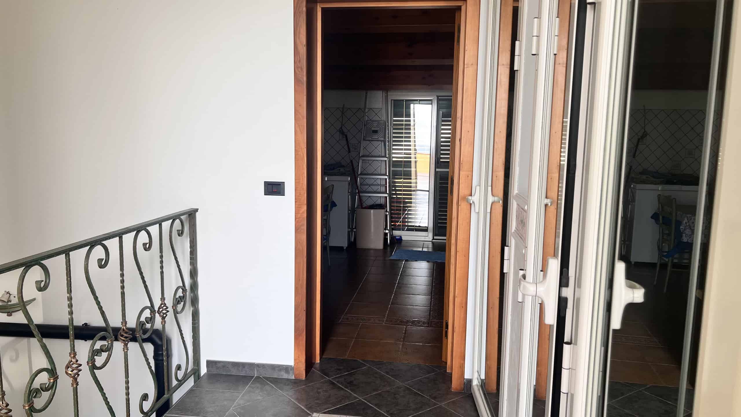 Ingresso di una villa unifamiliare con porta in legno e finestra, vista dall'esterno verso l'interno.