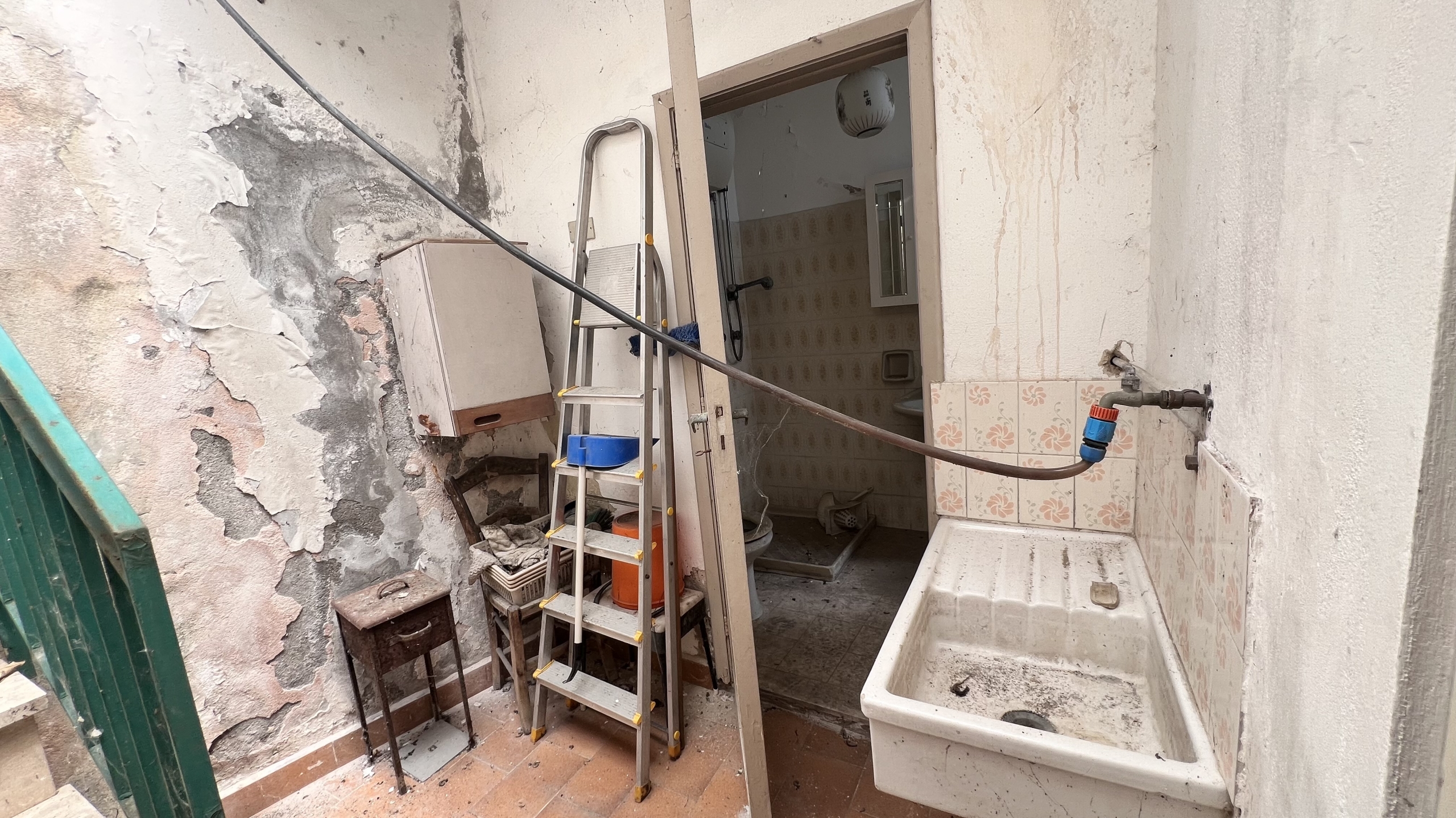 Interno di un appartamento in vendita a Scaletta Zanclea, con pareti danneggiate e un lavandino vecchio.