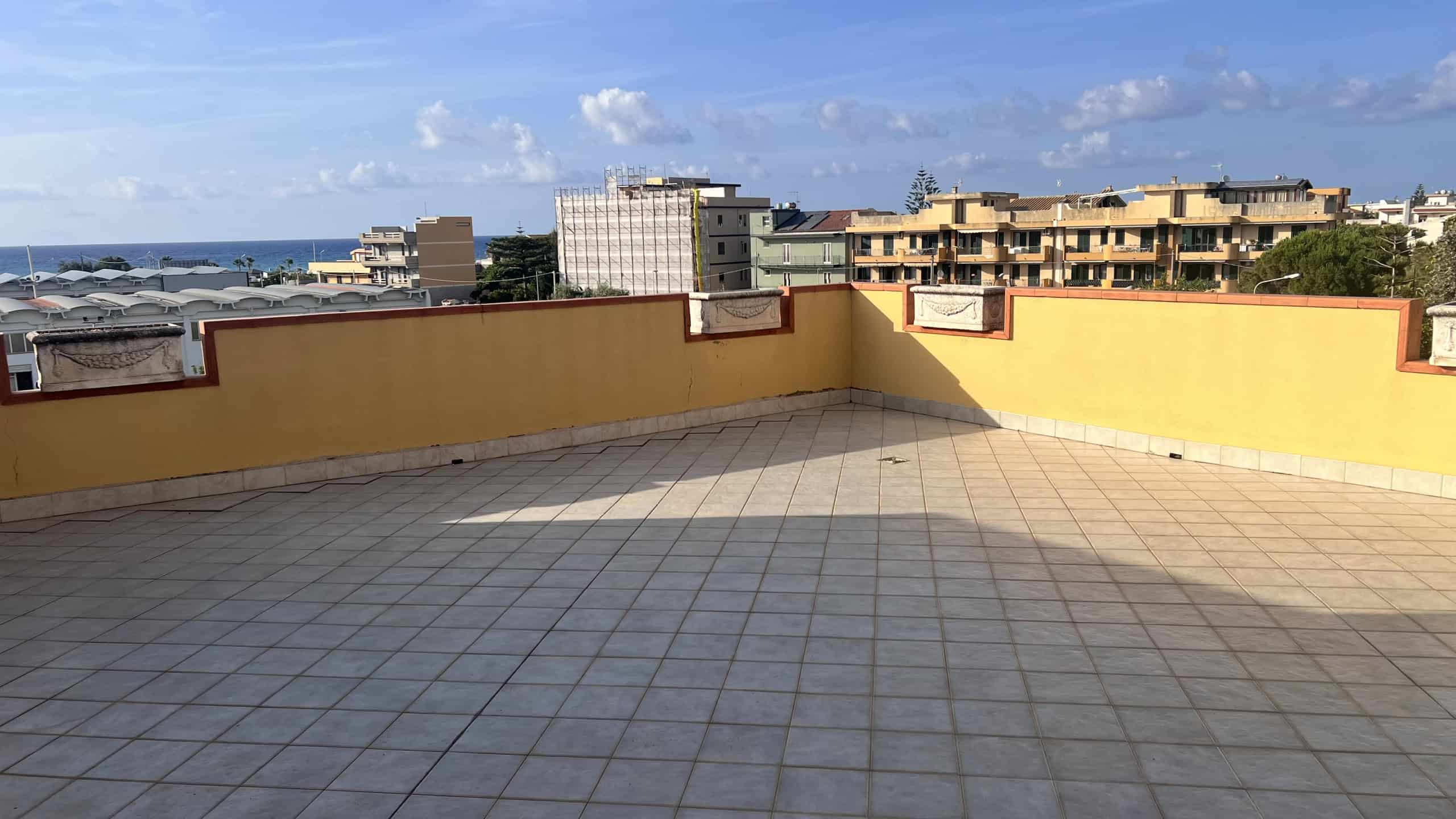 Terrazza panoramica con vista mare e città, pavimentata con piastrelle chiare, in un complesso residenziale a Villafranca Tirrena.