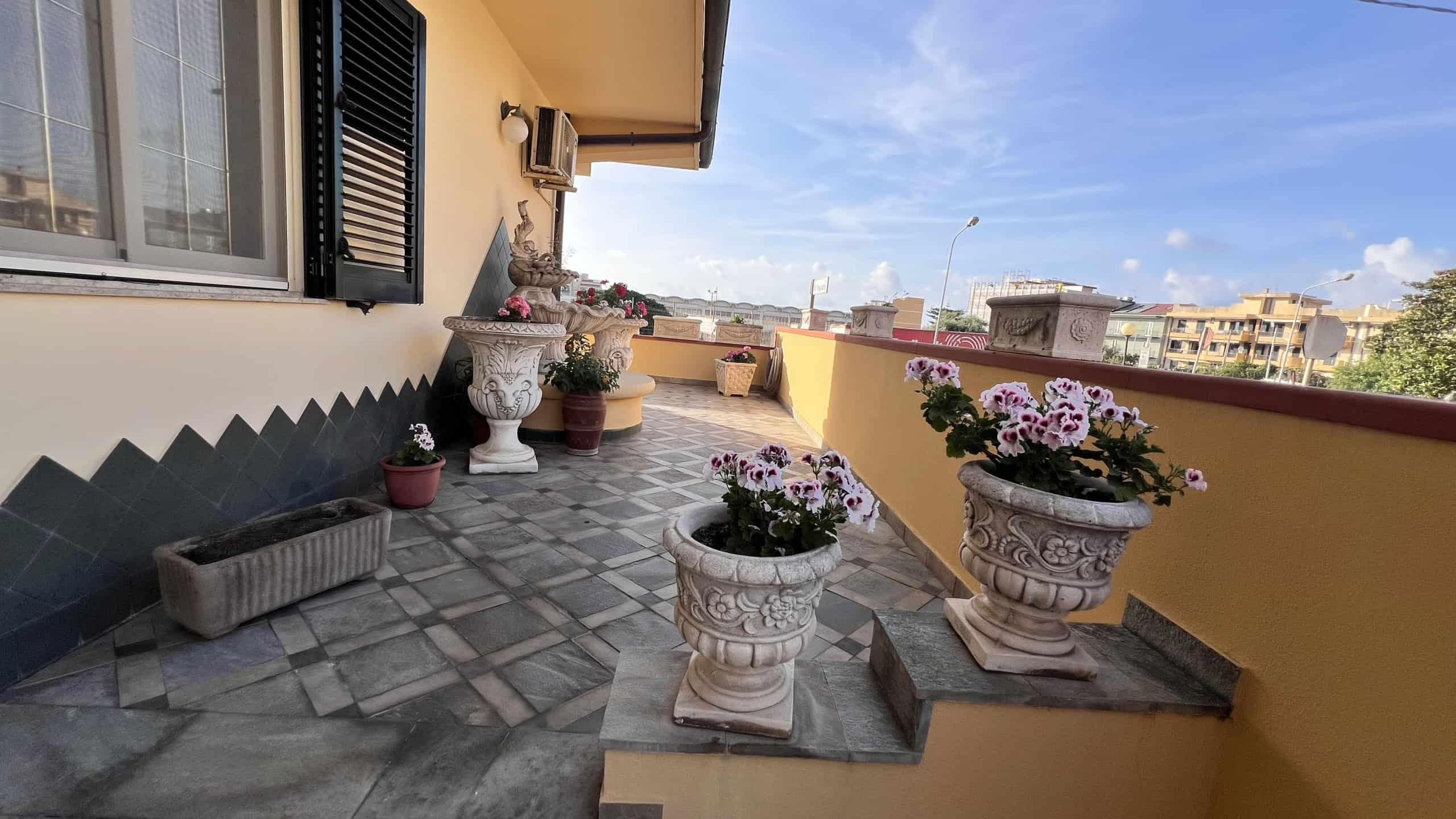 Balcone di un appartamento con fiori in vasi decorativi e vista sulla città di Villafranca Tirrena.