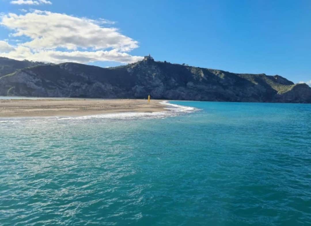 Spiaggia di sabbia con mare cristallino e sfondo montuoso a Falcone, Sicilia, perfetta per vacanze estive e relax.