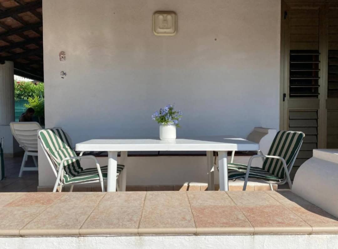 Veranda esterna con tavolo bianco e sedie con cuscini verdi e bianchi, ideale per relax e pranzi all'aperto in zona Falcone, Me.
