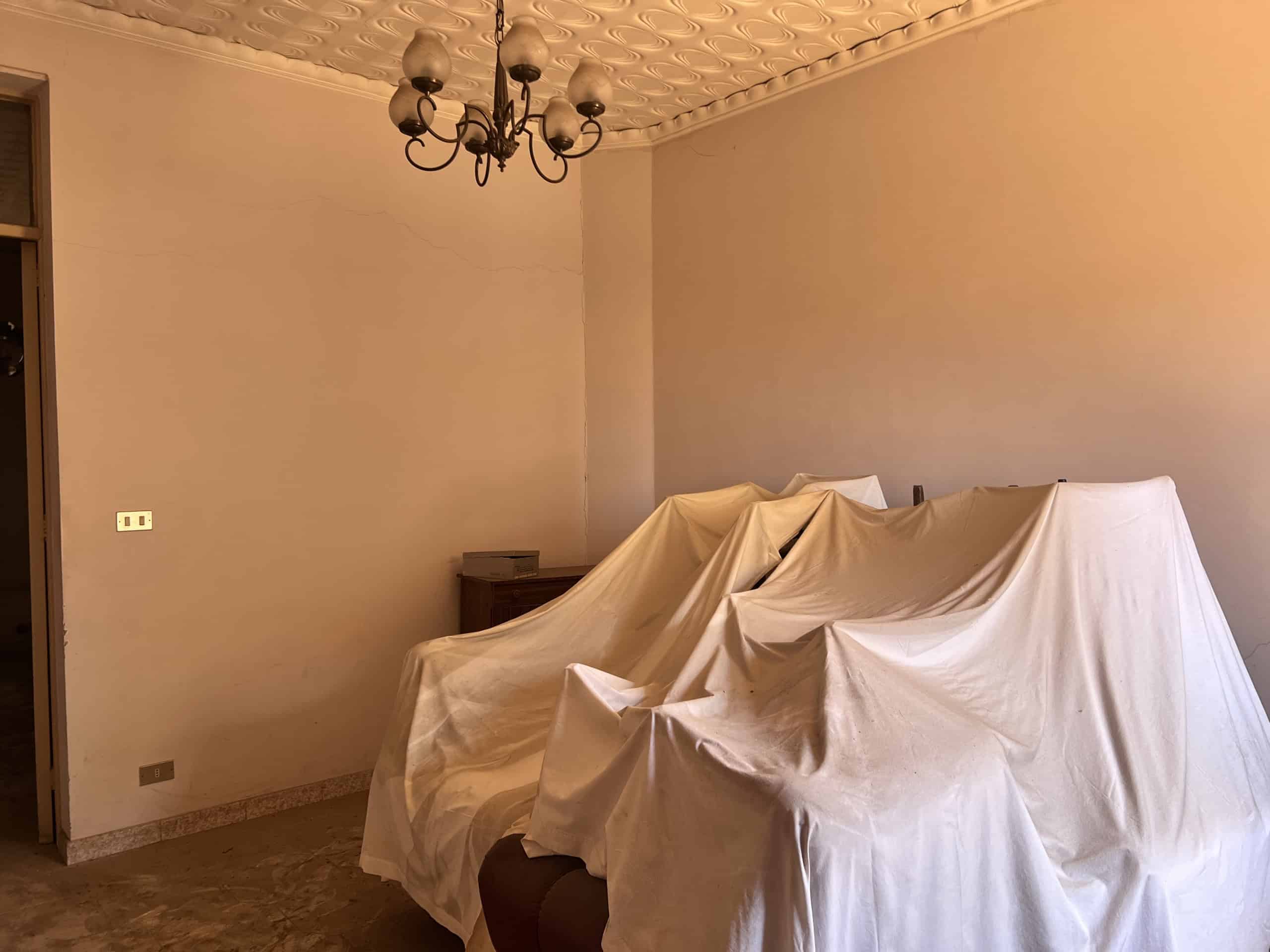 Salotto con mobili coperti da teli bianchi in un appartamento in vendita a Scaletta Zanclea, vicino a Messina.