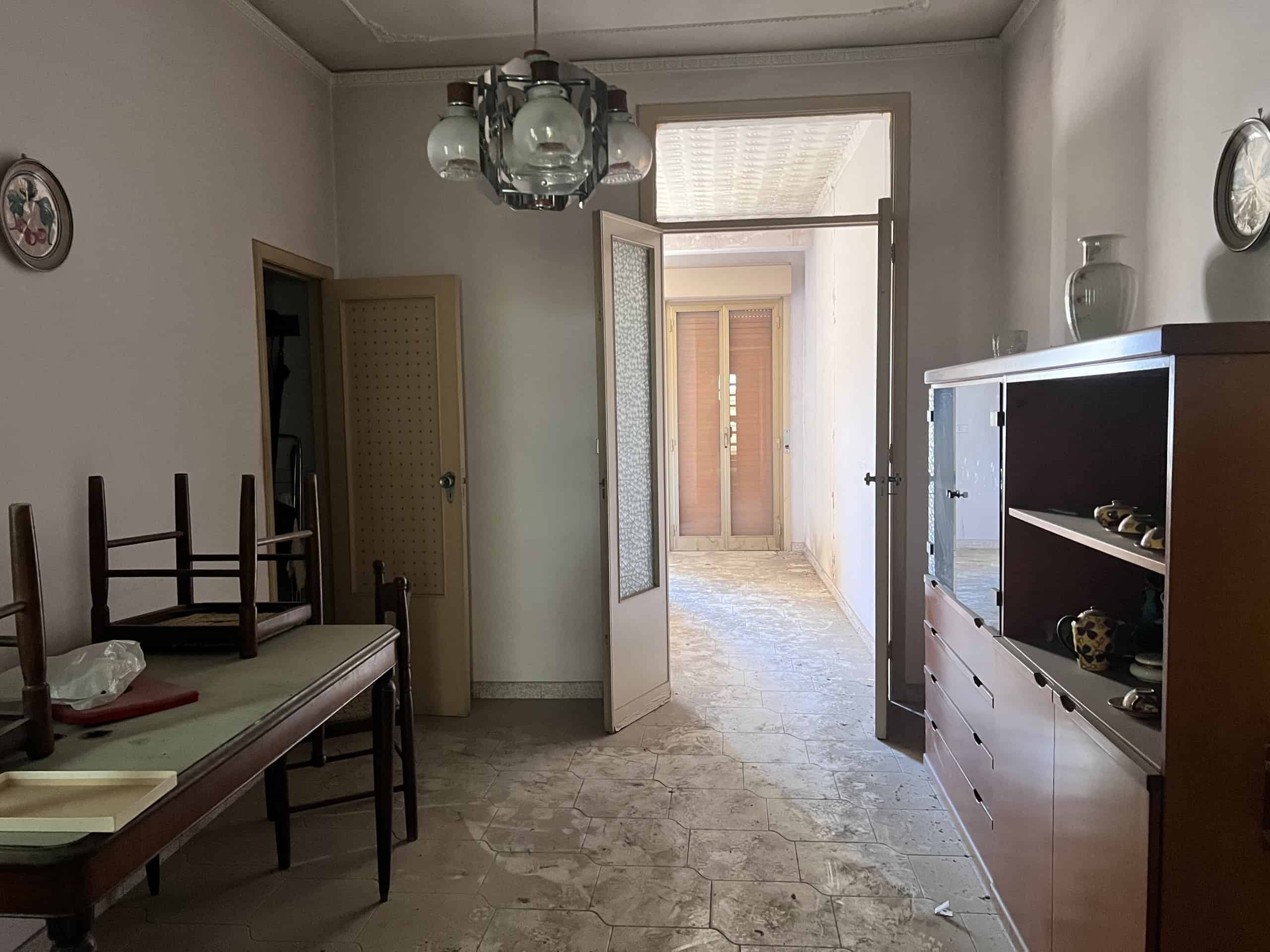 Interno di un appartamento con ingresso, mobili e porta finestra che conduce a un balcone, in vendita a Scaletta Zanclea, vicino a Messina.