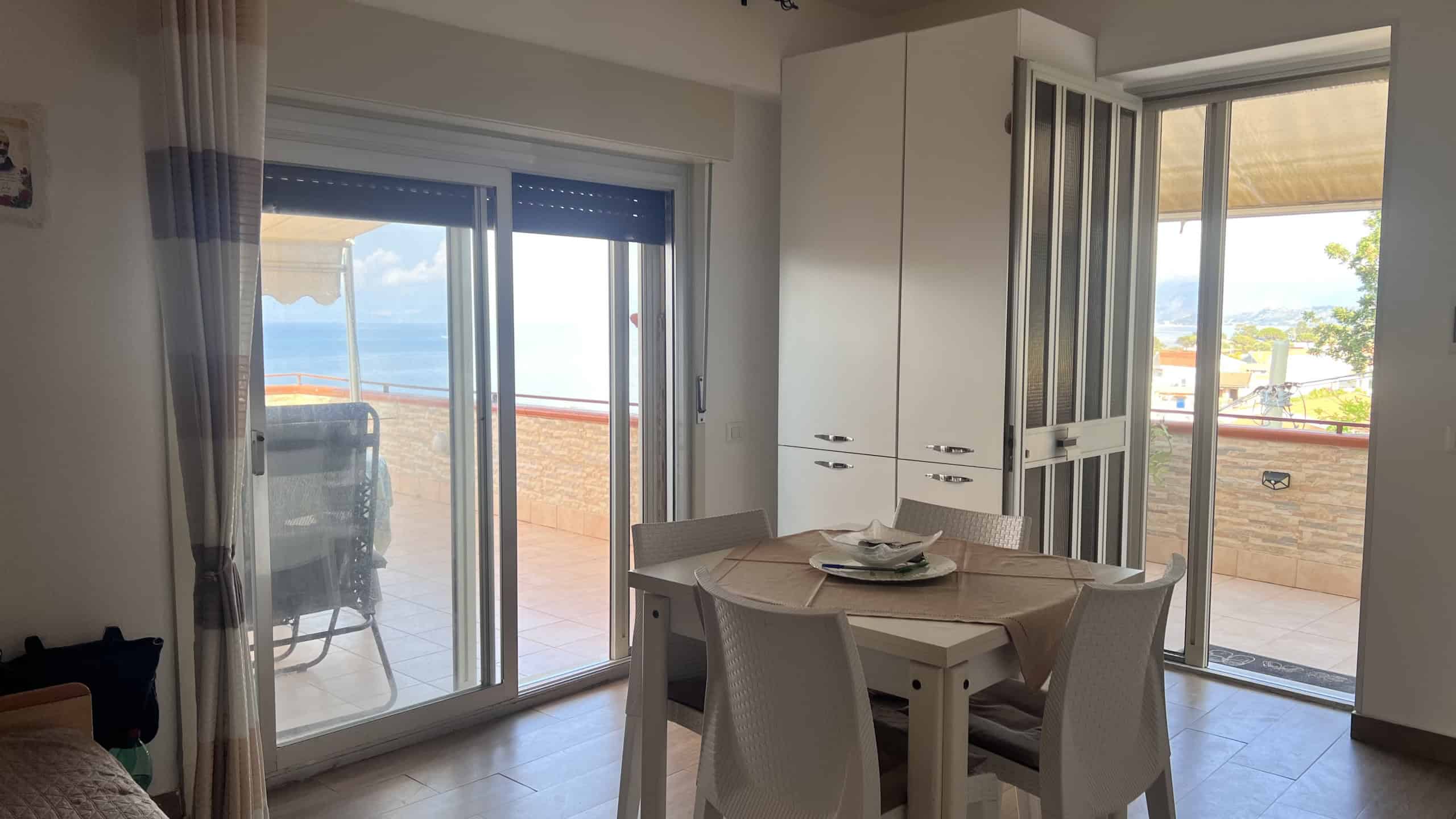 Interno luminoso di un appartamento con vista mare, con zona pranzo e accesso al balcone esterno.