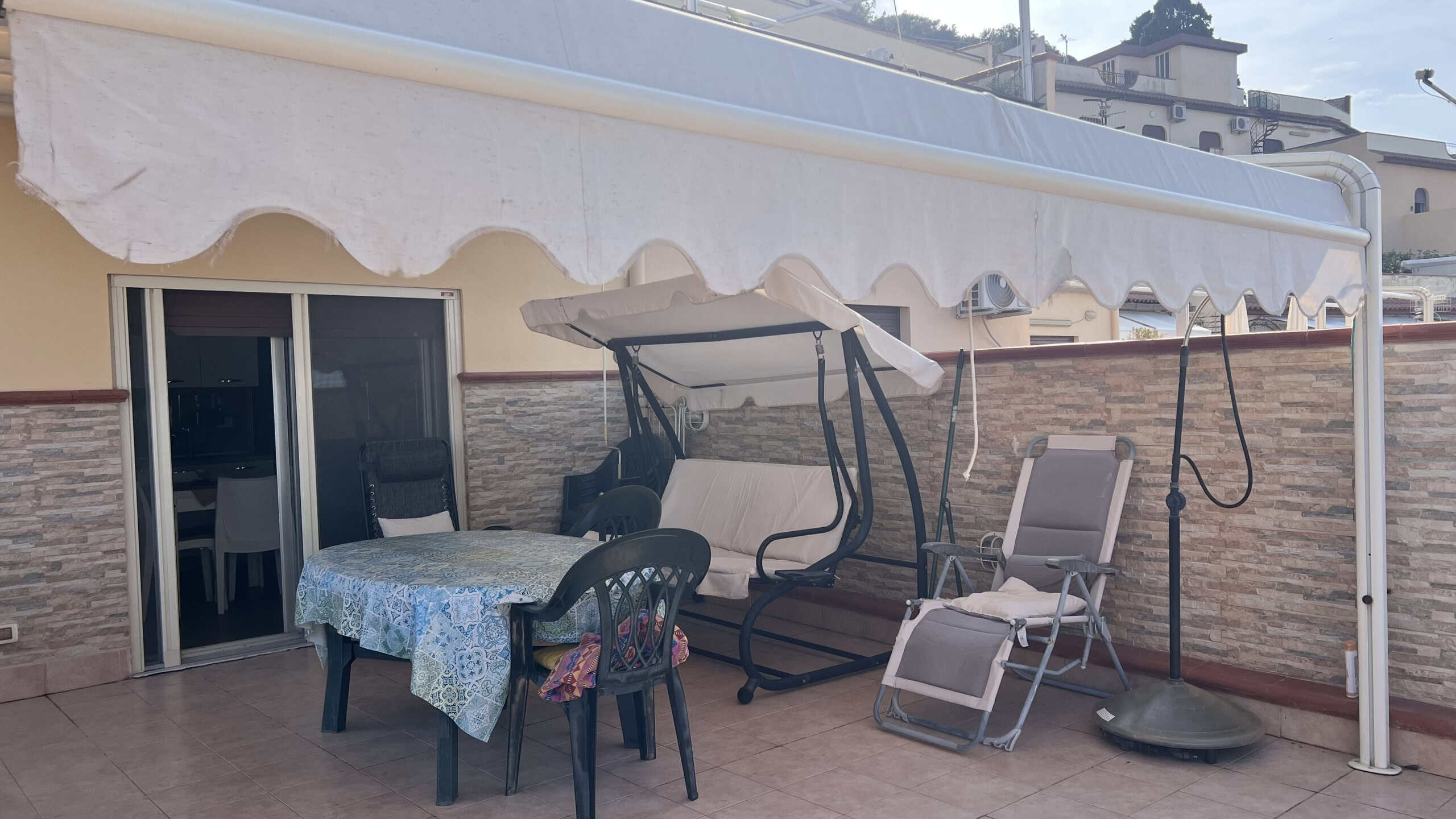 Spazio esterno con sedie, tavolo, dondolo e ombrellone, ideale per relax all'aperto in zona residenziale di Acqualadroni.