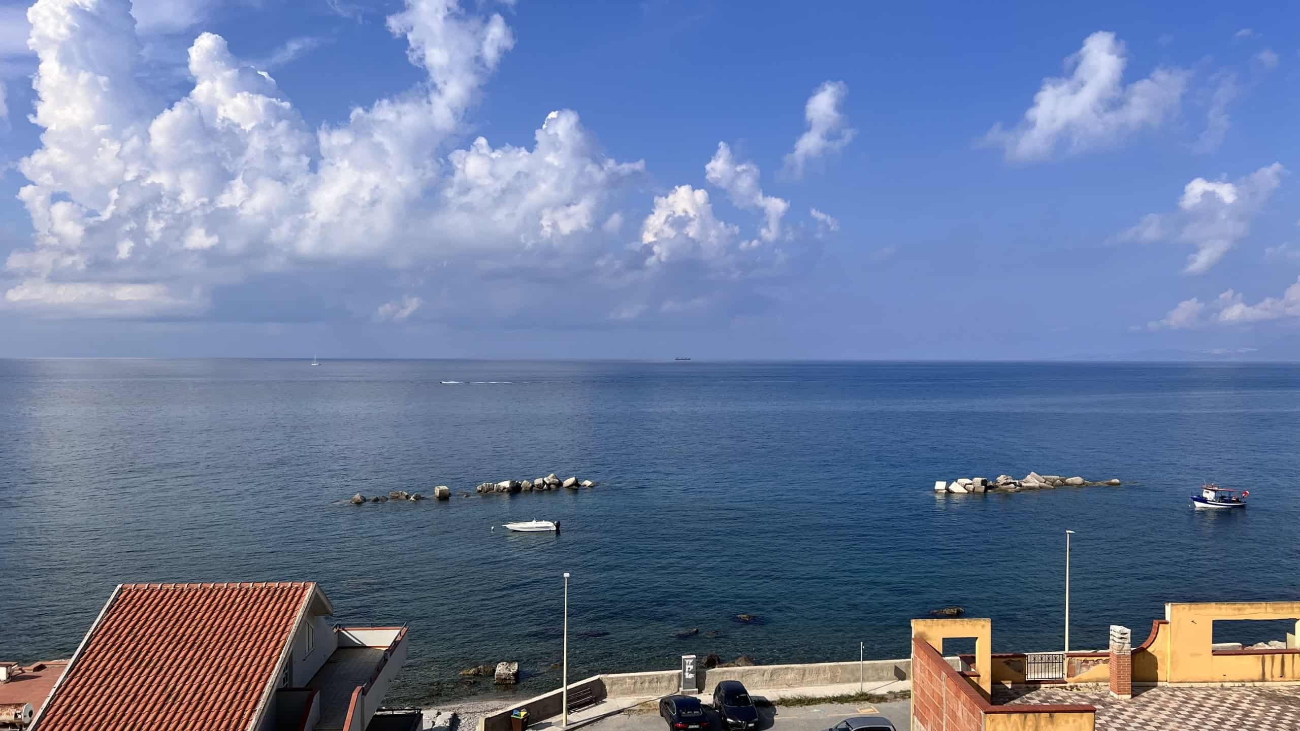 Vista panoramica sul mare con cielo sereno, barche e scogli, vista dall'appartamento in Via Del Corsaro 81, Acqualadroni, Me.
