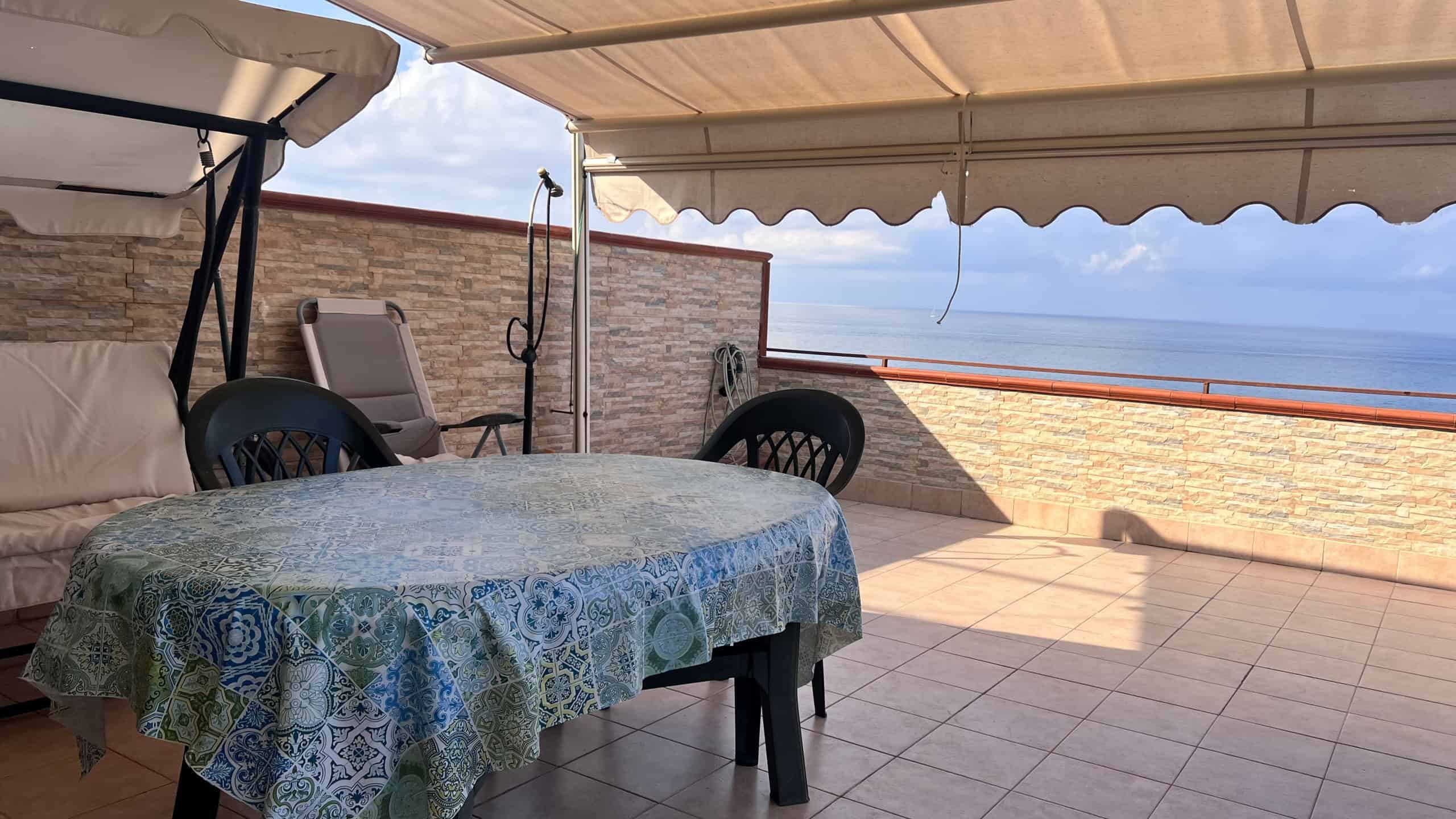 Terrazza con tavolo e sedie, vista panoramica sul mare, spazio esterno in Acqualadroni, Me.