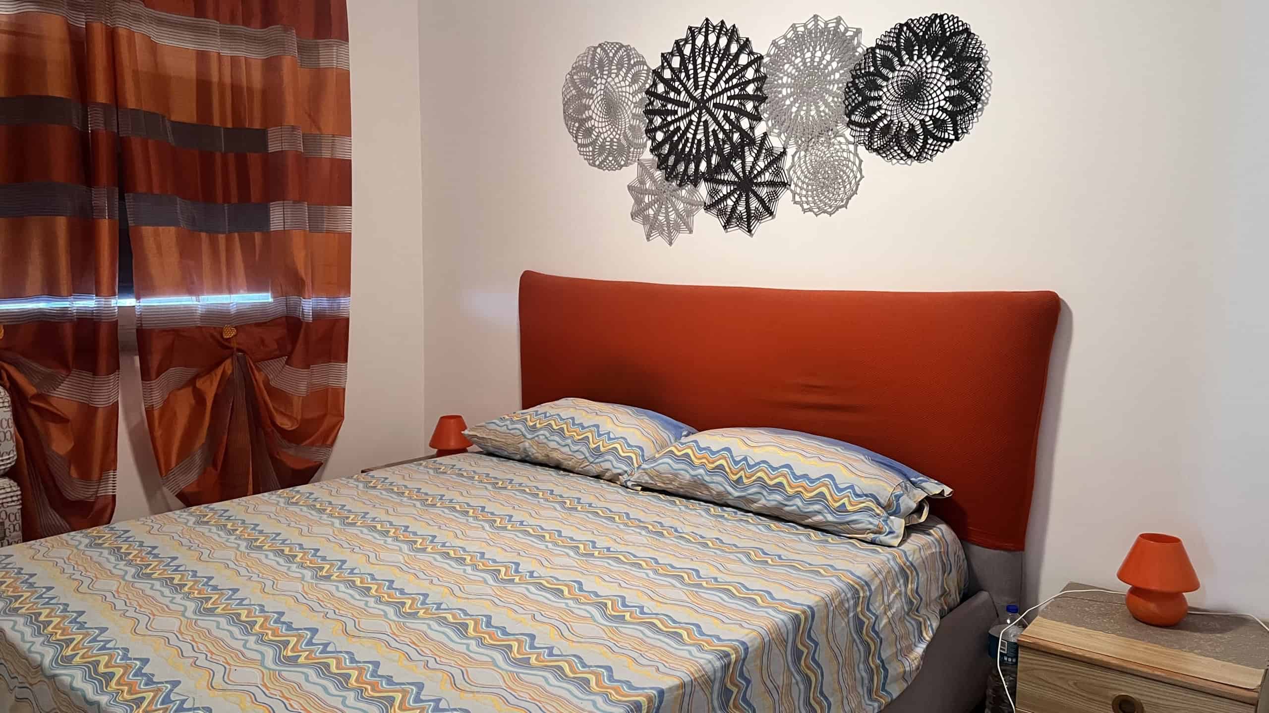 Camera da letto con parete decorativa, letto con testiera arancione e tende a righe colorate.