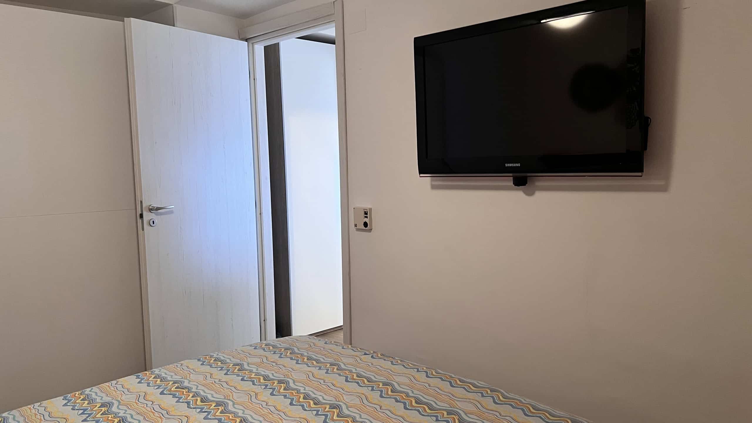 Televisore a schermo piatto montato sulla parete in una camera da letto moderna con letto e porta aperta.