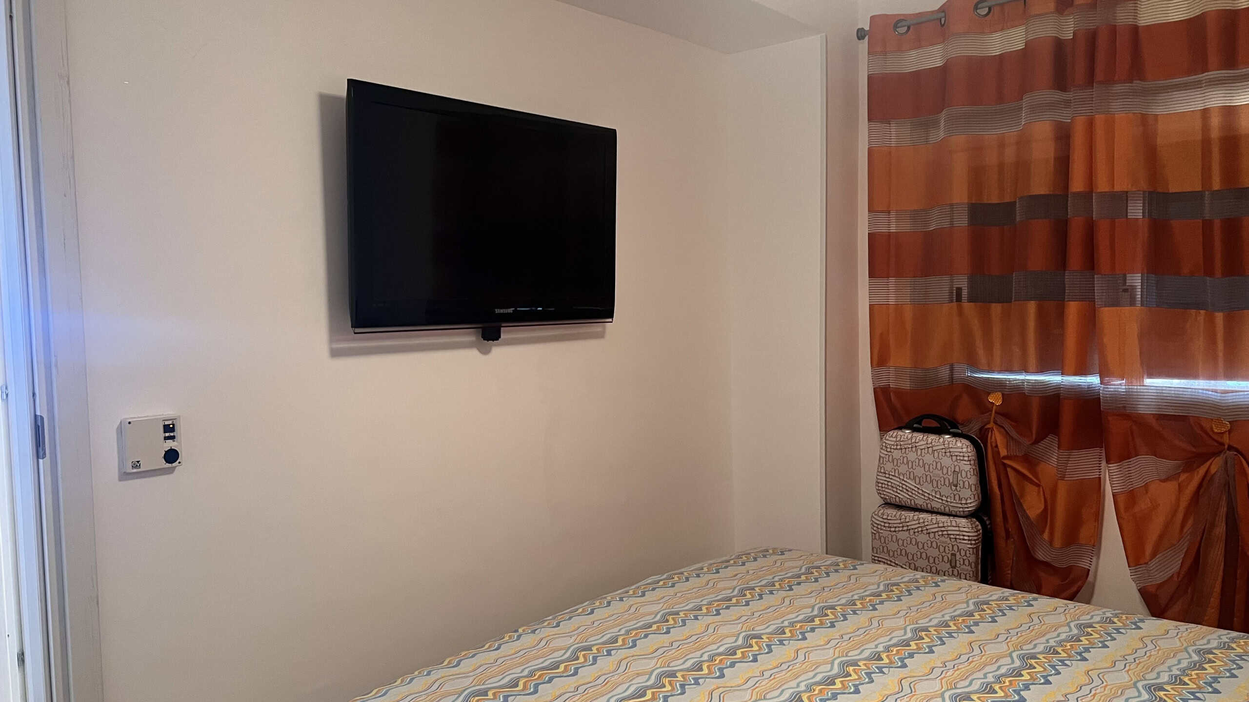 Televisore a schermo piatto montato sulla parete in una camera da letto con letto e tende colorate.