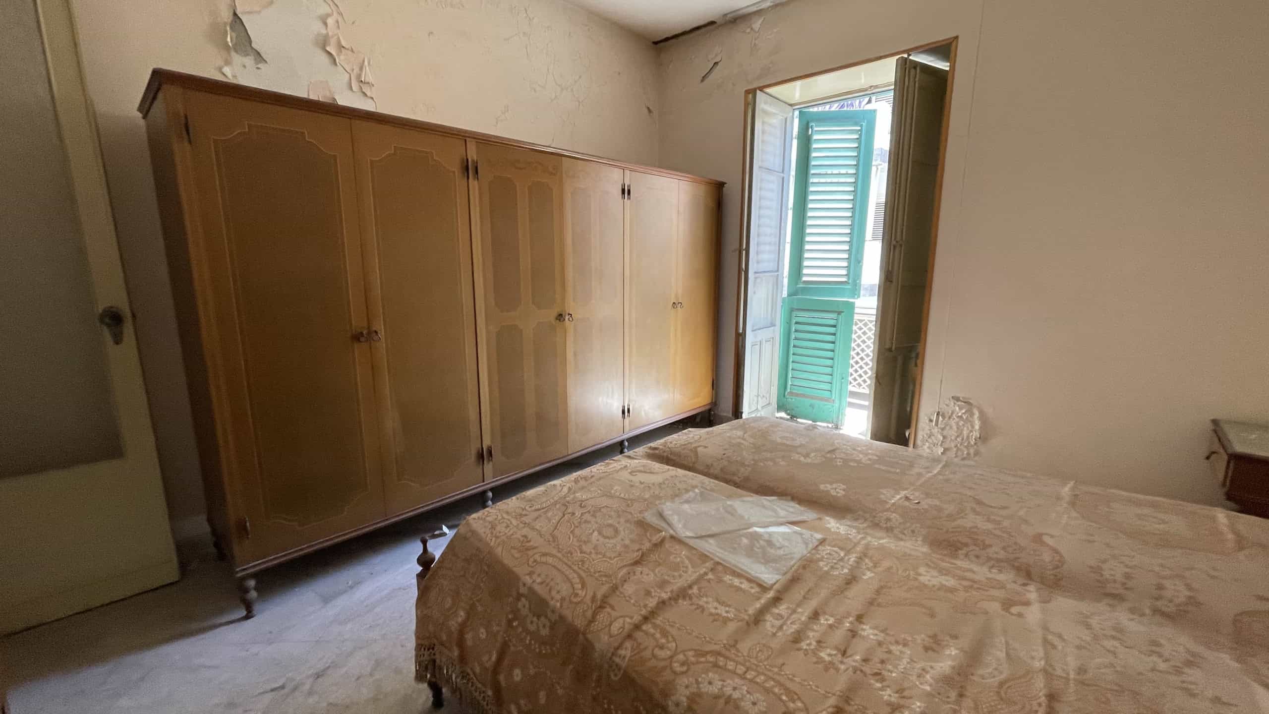 Camera da letto con armadio in legno e finestra con persiane verdi, ambiente luminoso e spazioso in Scaletta Zanclea, Me.