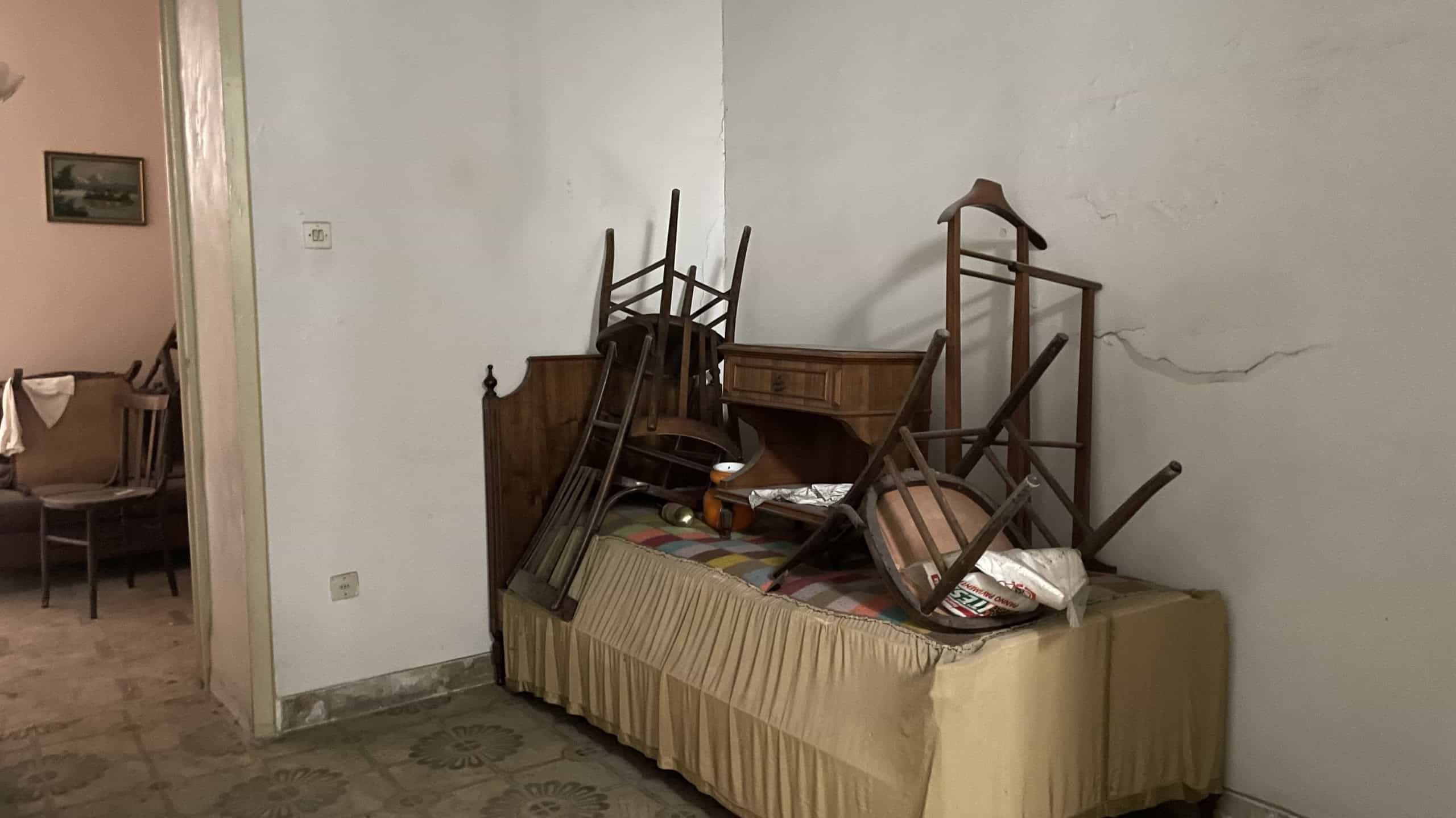 Mobili vecchi e disordinati in soggiorno, con sedie e tavolo impilati, in una casa in vendita a Scaletta Zanclea, Me.