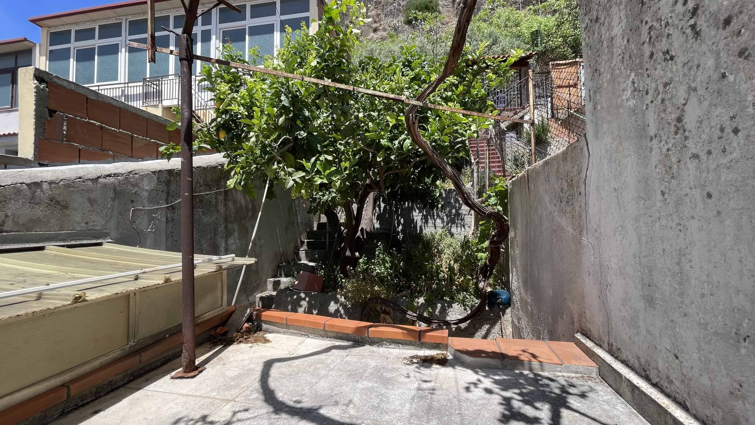 Cortile esterno con piante e area di servizio, vicino a un edificio residenziale a Scaletta Zanclea, Me.