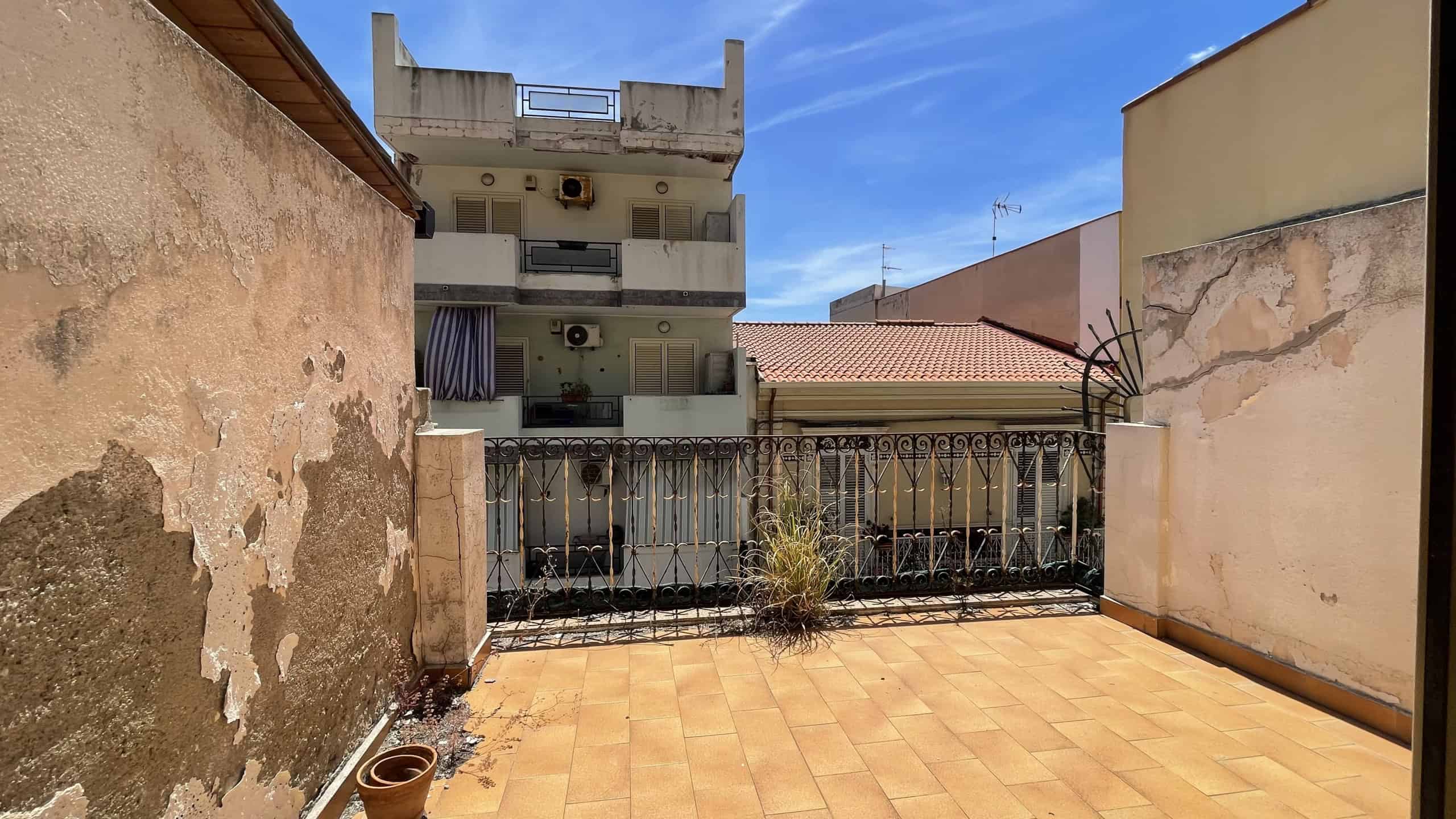 Balcone con vista sulla città e sul cielo azzurro, con pavimentazione in piastrelle e pareti in muratura.
