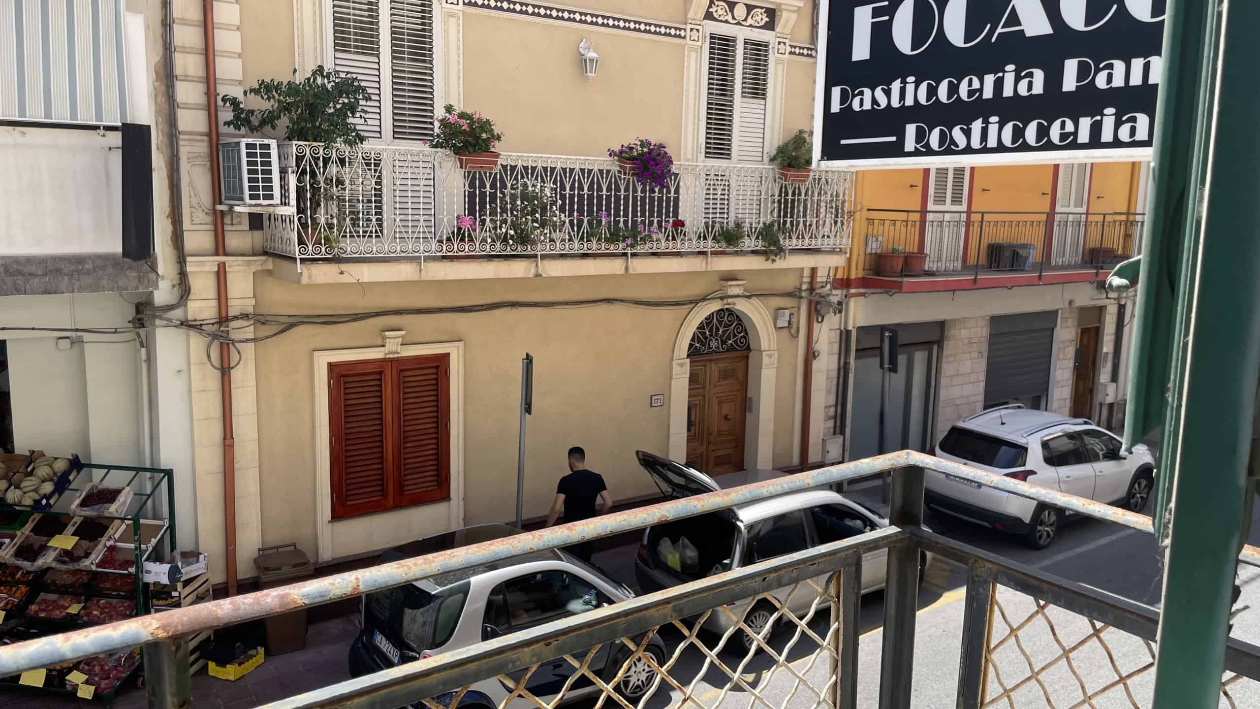 Immagine di un edificio residenziale a Scaletta Zanclea con balconi fioriti e auto parcheggiate sulla strada.