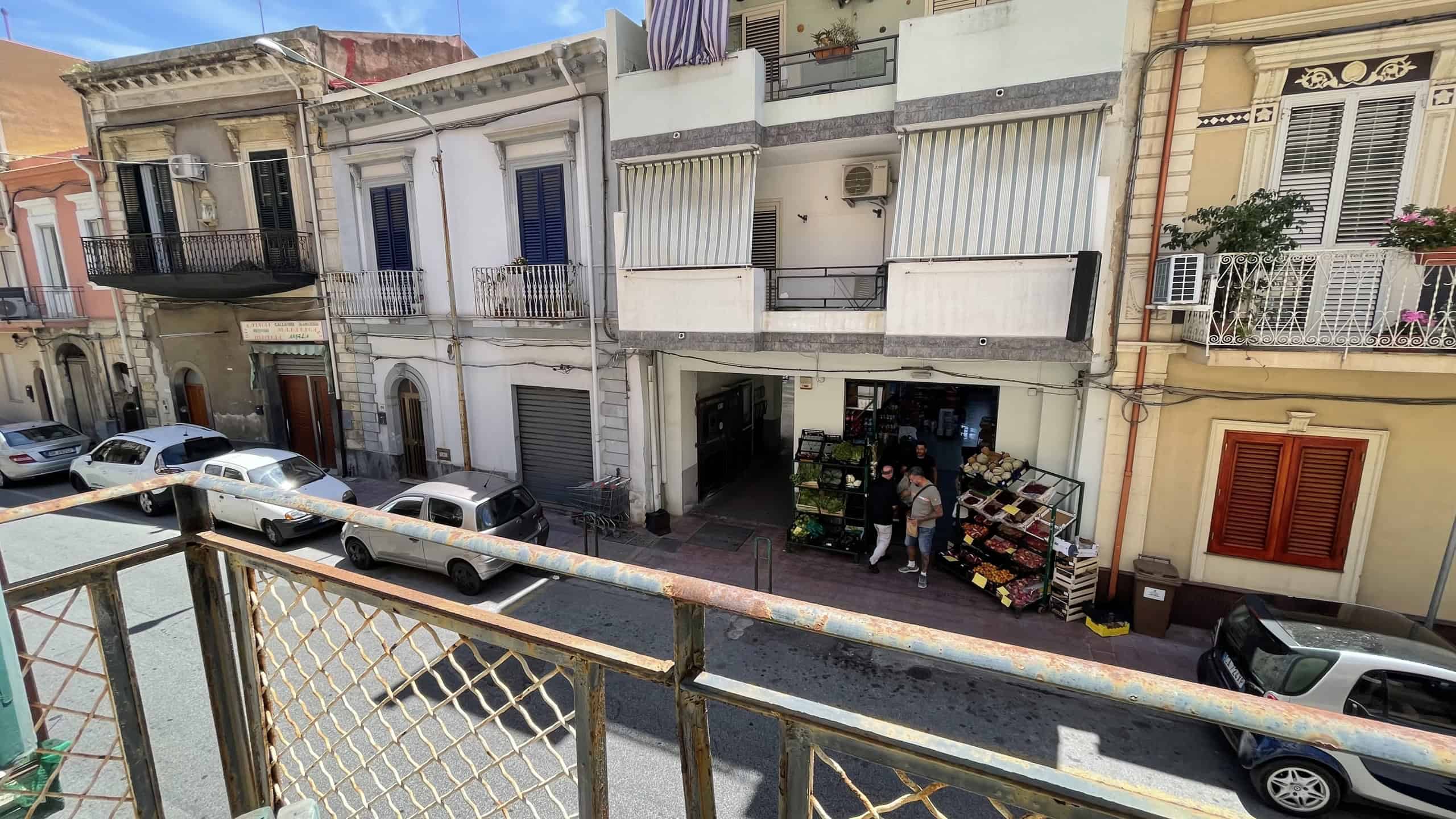Vista di un edificio residenziale in Via Roma 168 a Scaletta Zanclea, con negozio al piano terra e balconi al primo piano, parcheggio e auto in strada.