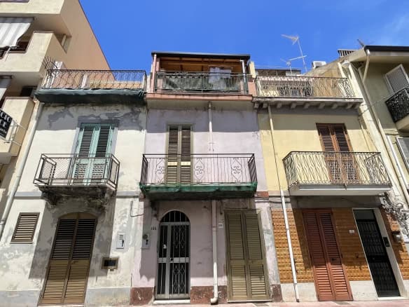 Facciata di un edificio residenziale in Via Roma 168, Scaletta Zanclea, con balconi e finestre, sotto un cielo blu.